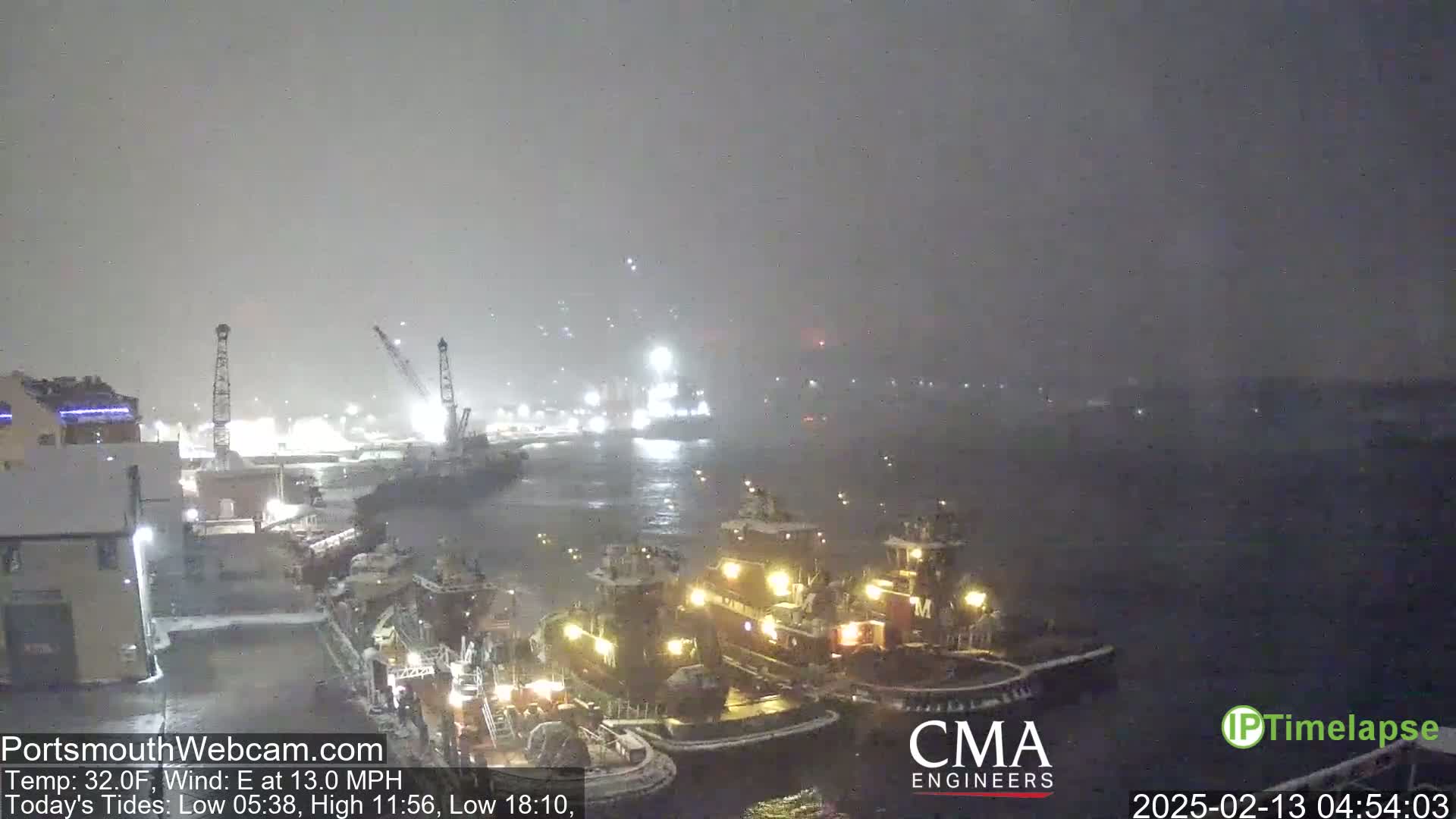 Several tugboats are moored in a harbor during a nighttime snowstorm.