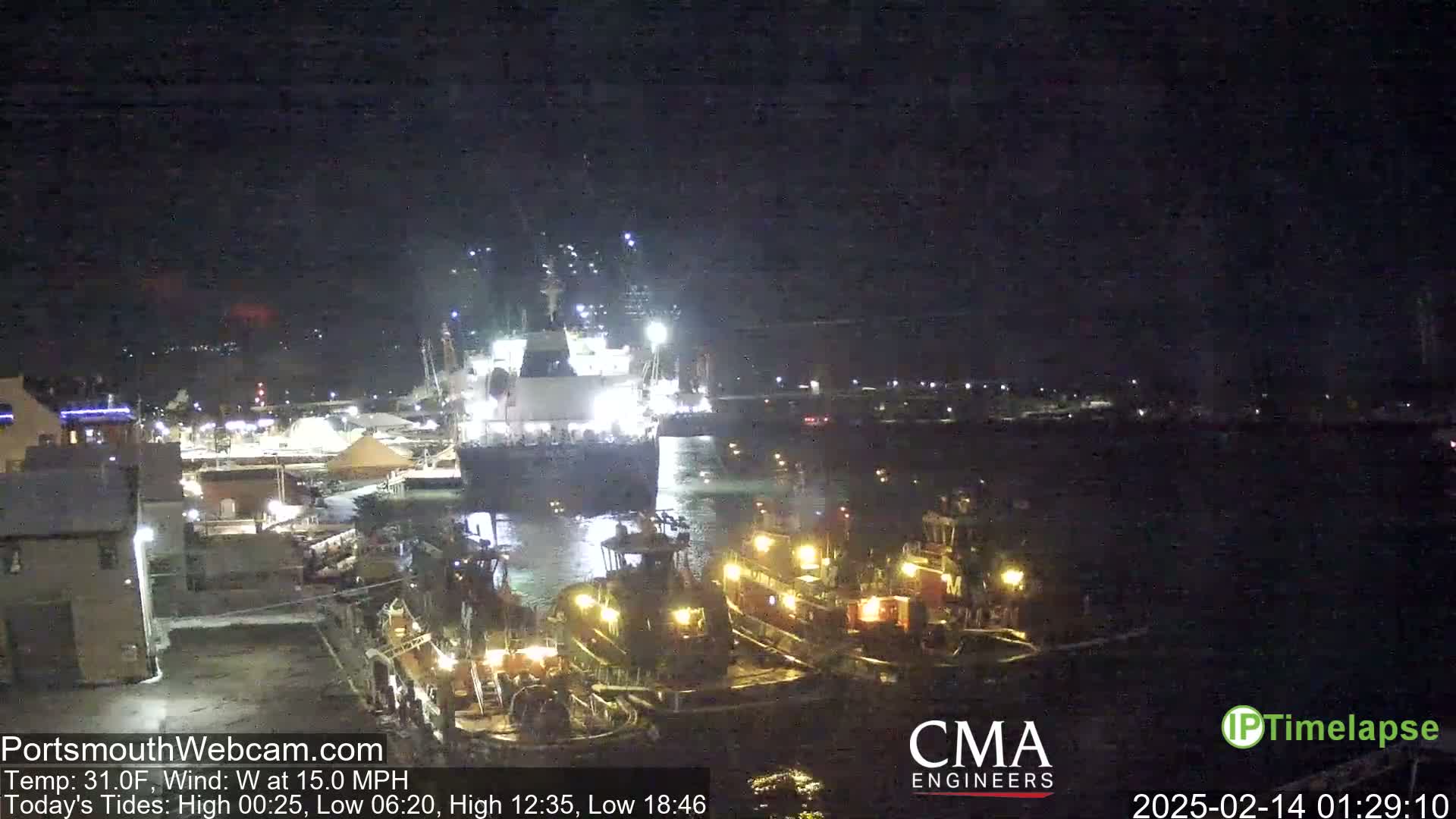 A large ship is being assisted by several tugboats in a harbor at night, with a west wind blowing at 15 miles per hour.
