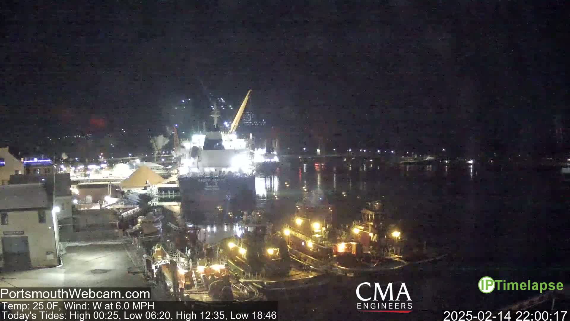 A large ship is docked at night near several smaller tugboats, under a clear, dark sky.
