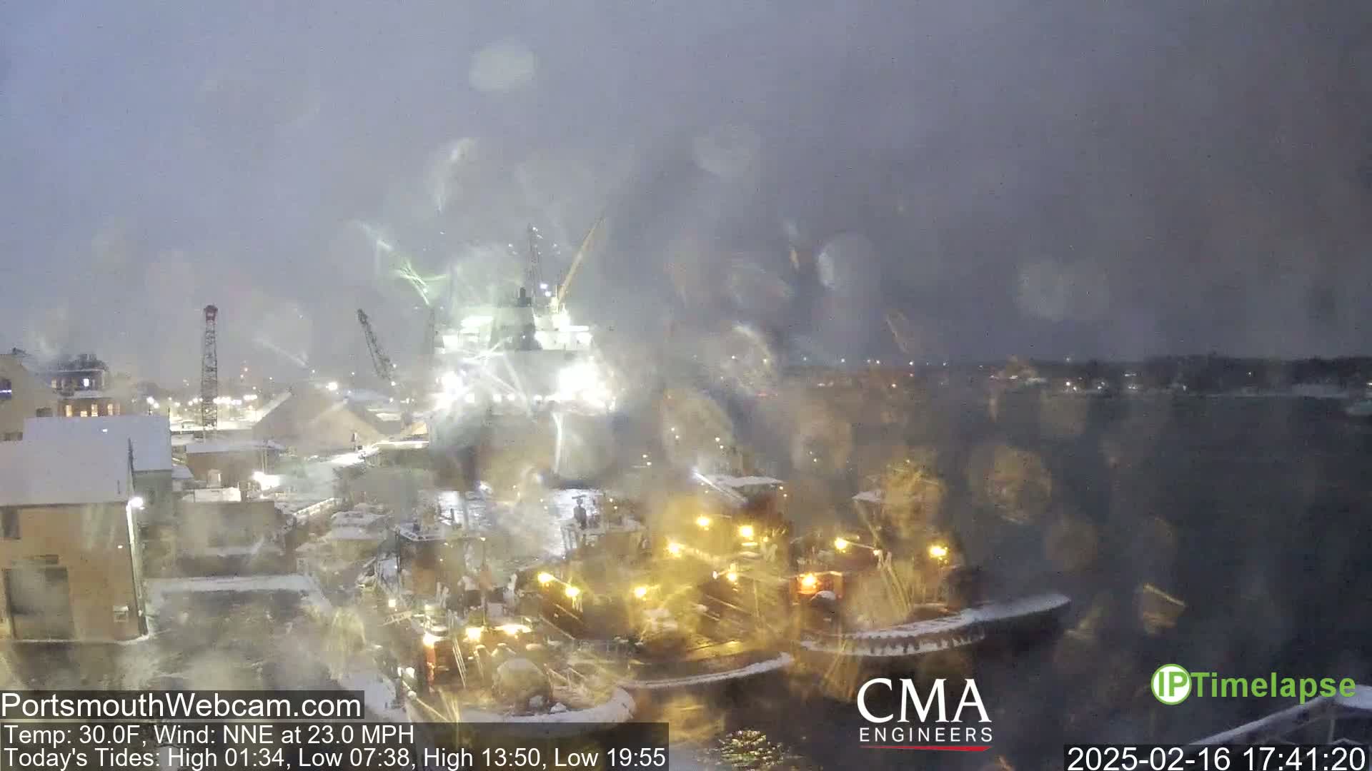 A large ship is being assisted by tugboats in a snowy harbor at night.