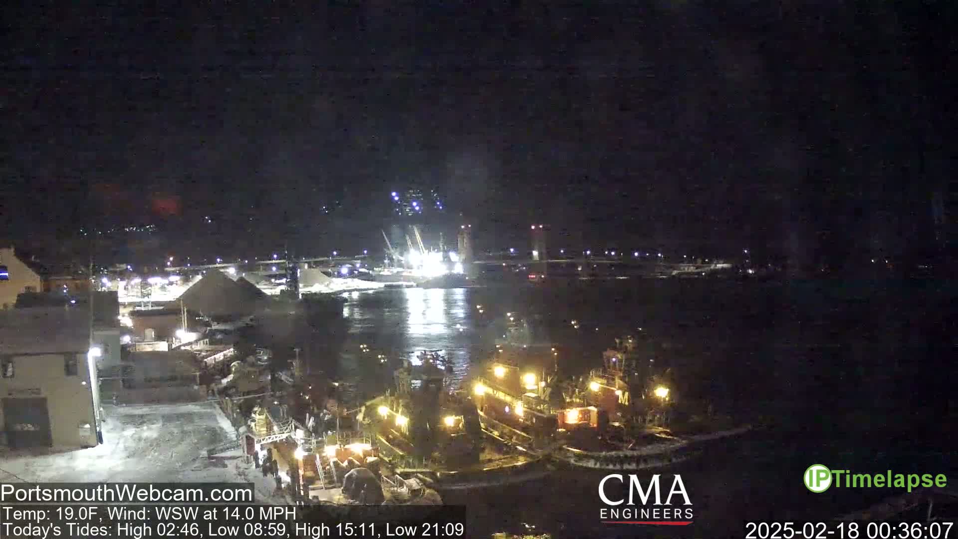 Several tugboats are illuminated at a nighttime harbor under a clear, dark sky with a moderate wind.