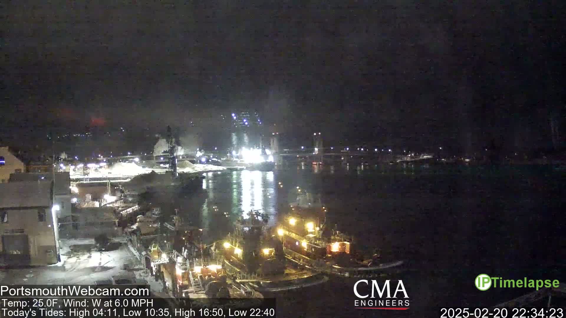 At night, two tugboats are moored near a waterfront industrial area under a dark sky.