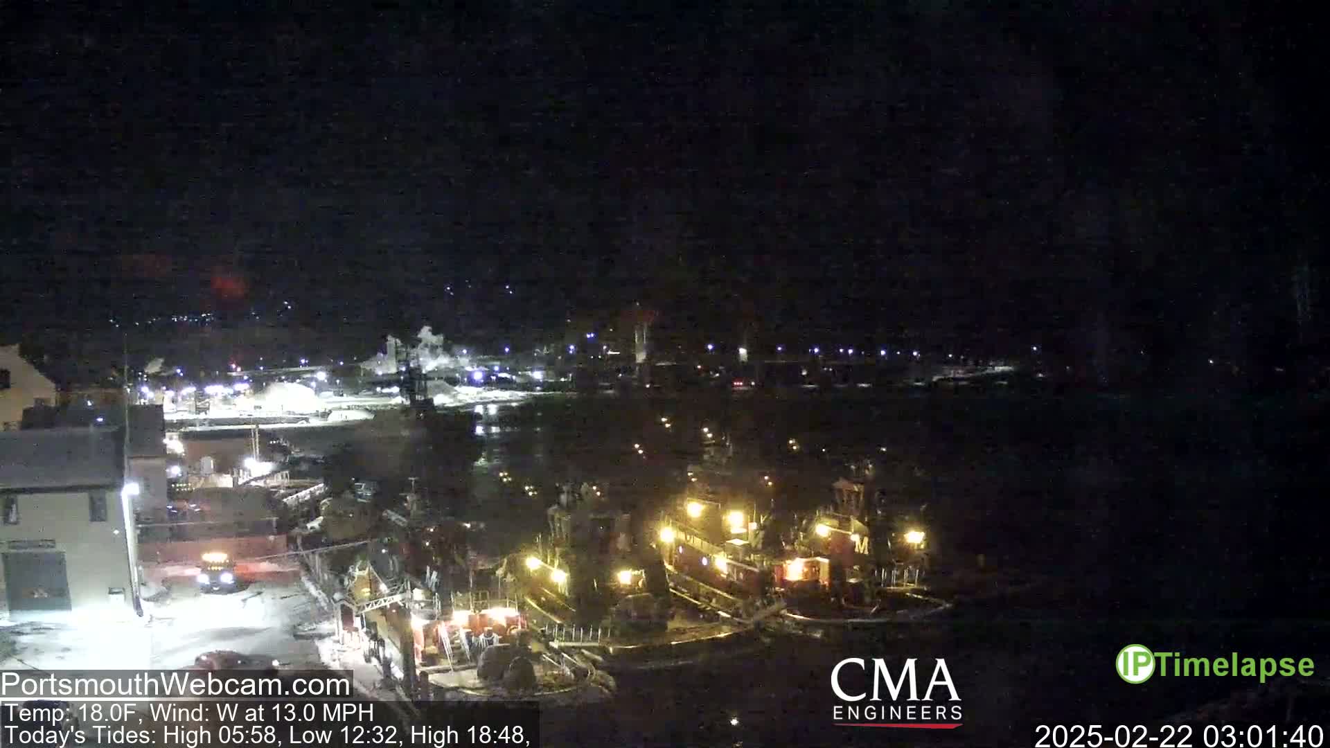 Several tugboats are moored at a dock at night, under a dark sky.