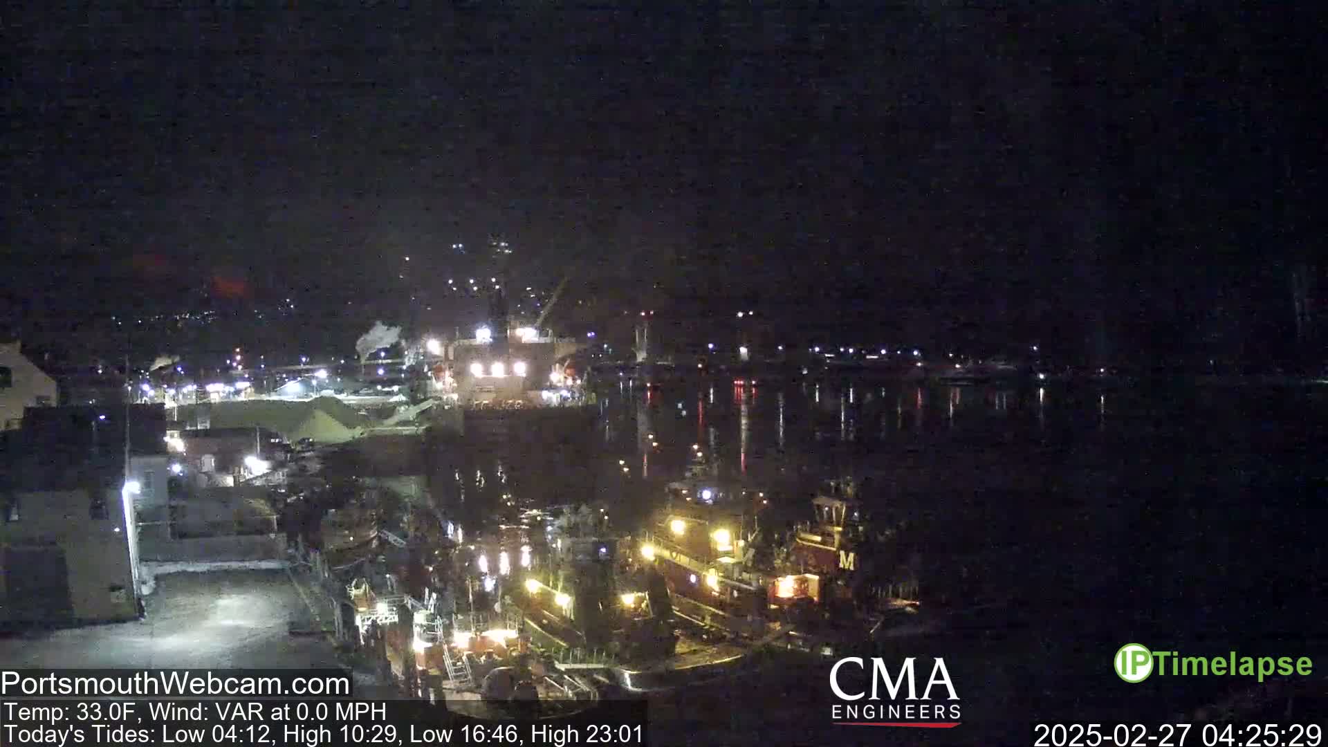 A nighttime harbor scene shows several boats docked along a pier, with calm water reflecting lights across the dark surface.