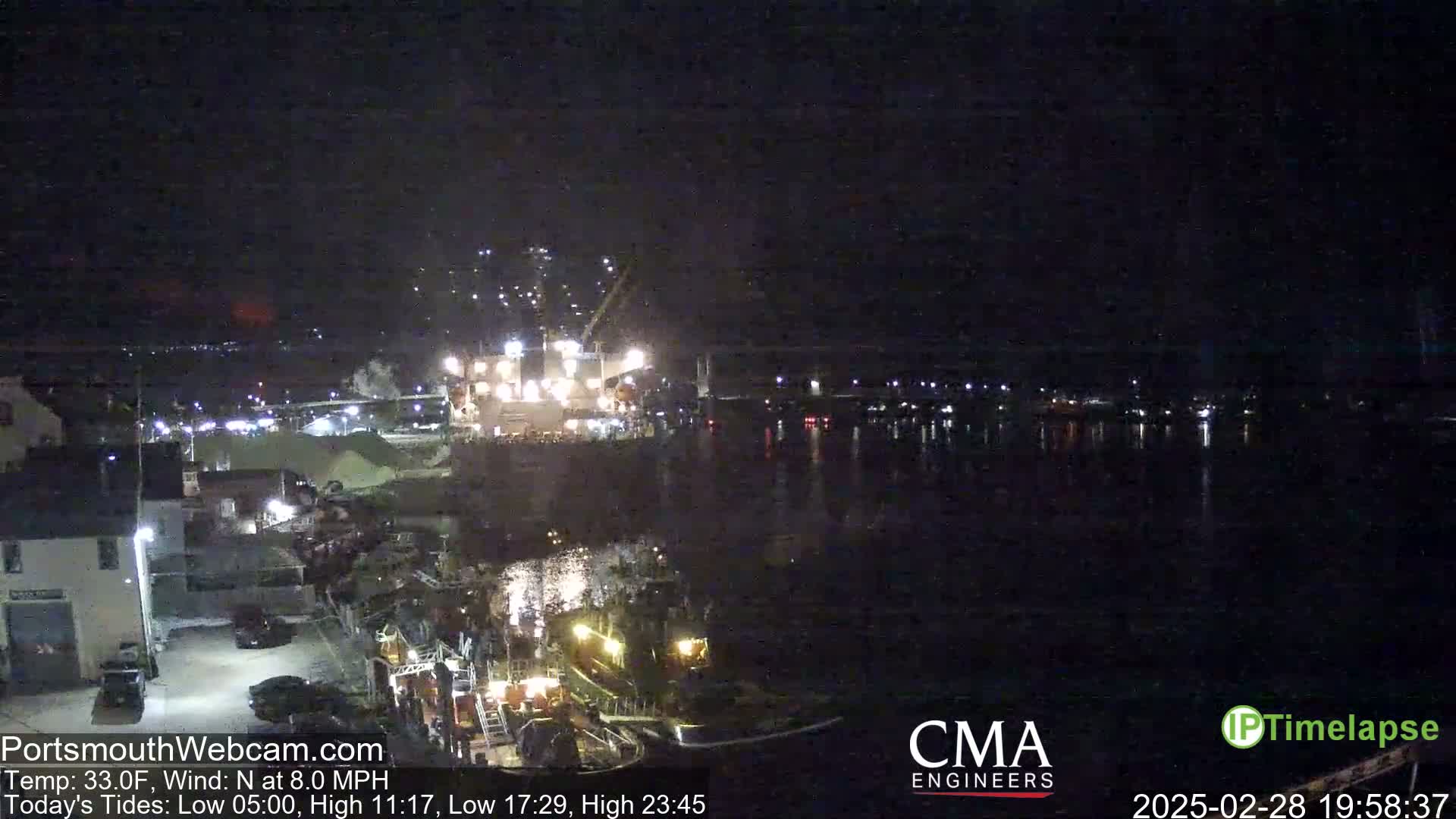 A nighttime harbor scene shows several lit vessels near a waterfront, with faint lights visible across the water under a dark, clear sky.
