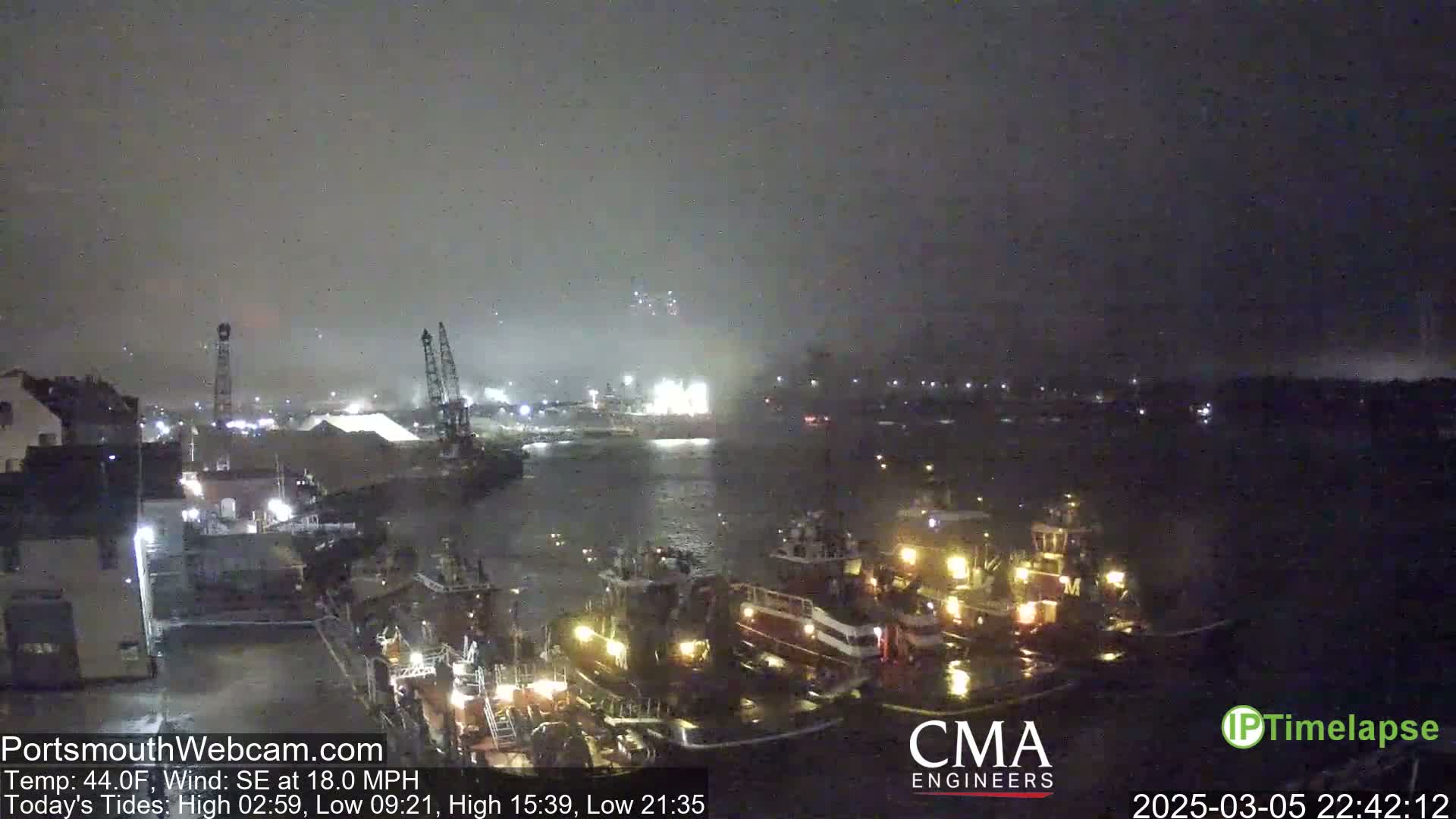 A nighttime harbor scene shows several tugboats moored near a dock under a dark, overcast sky with a southeast wind.