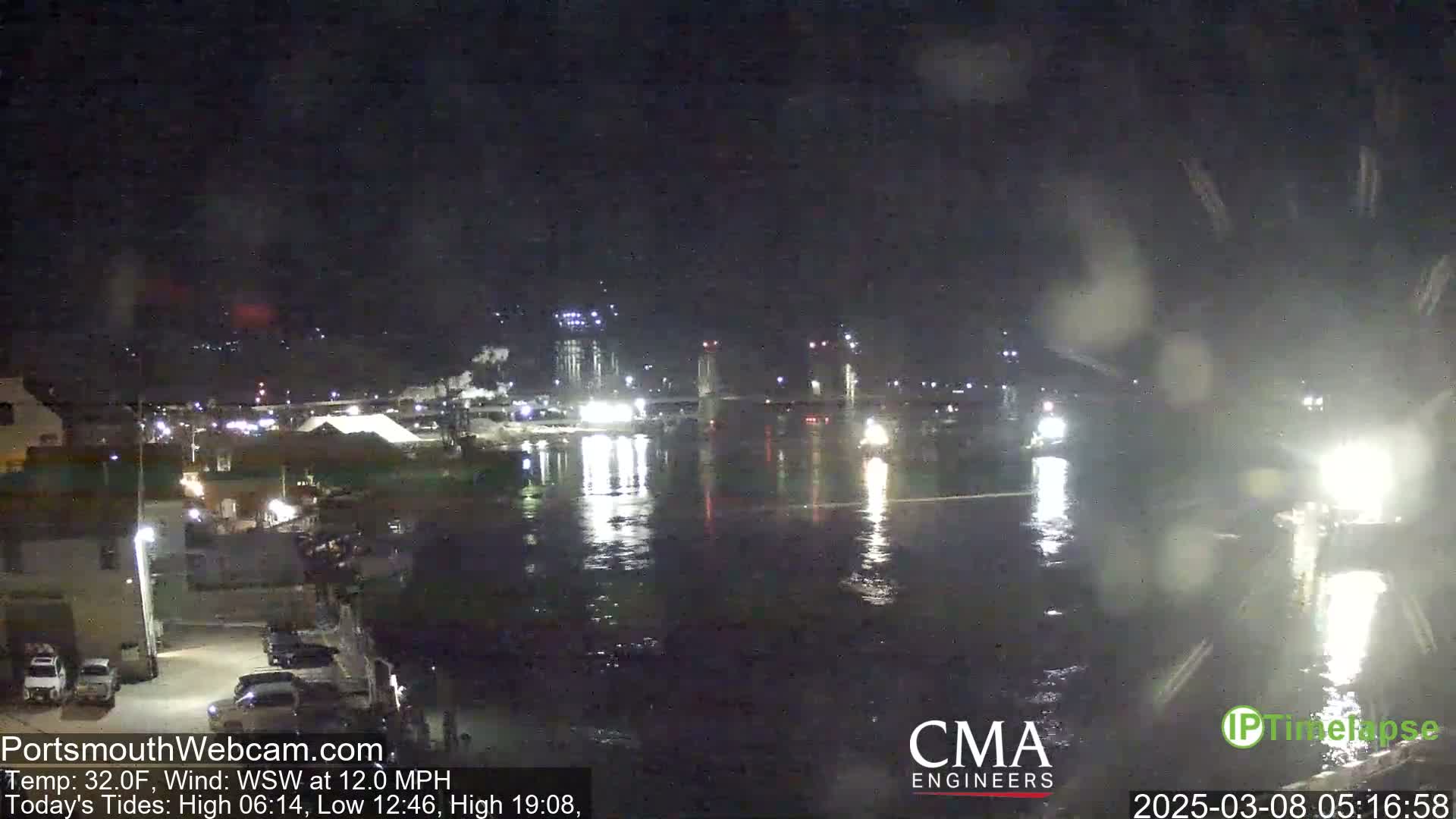 A nighttime view of a calm body of water reflecting city lights under a dark, possibly slightly snowy or rainy sky.