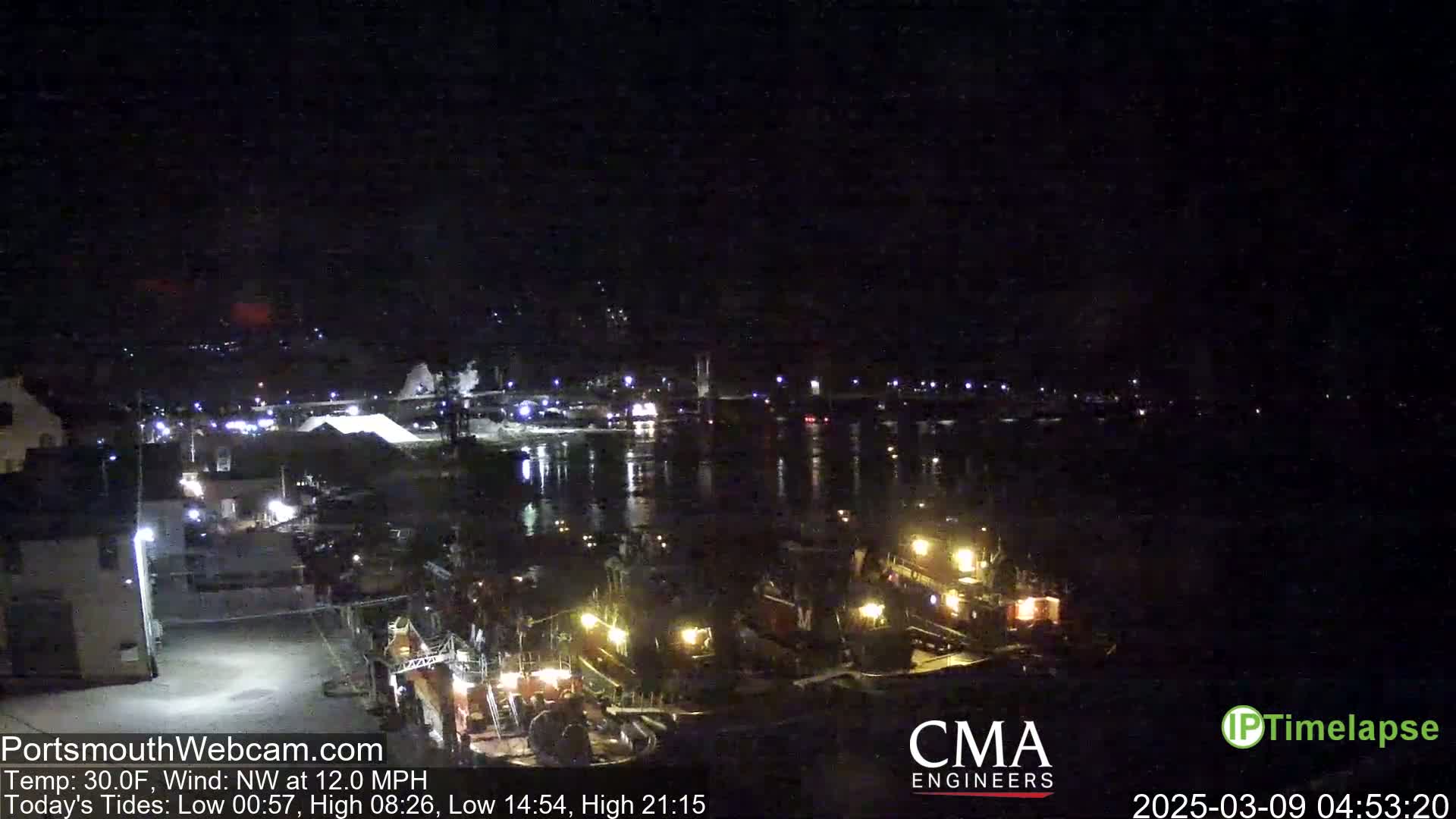 A nighttime view of a harbor with several docked boats illuminated by lights, under a clear, dark sky.