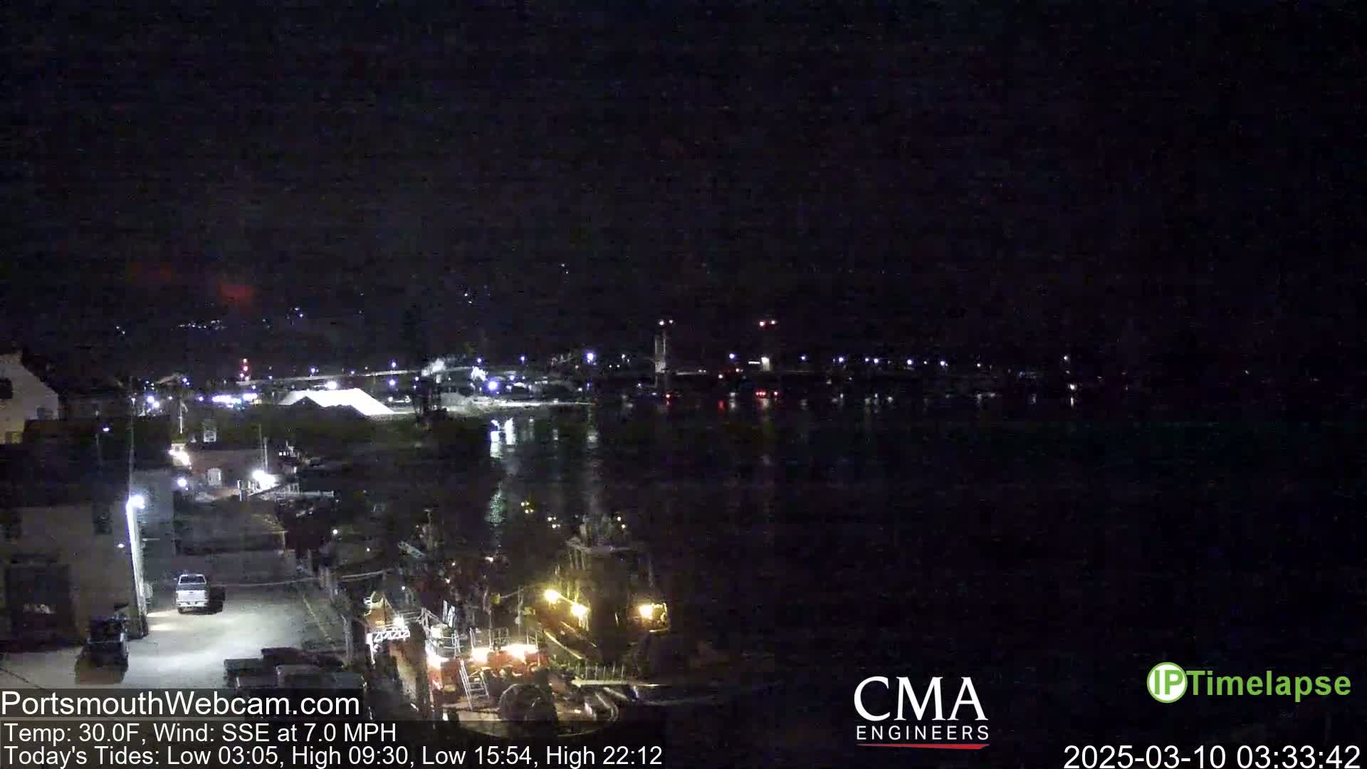 A nighttime view of a harbor with a few lights visible along the waterfront and a dark, calm body of water under a clear, dark sky.