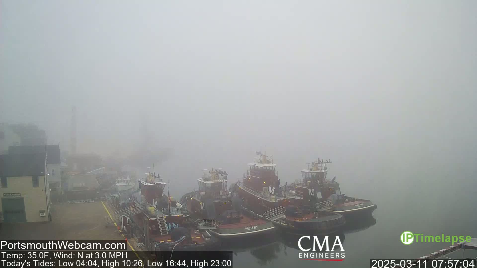 Several tugboats are moored at a dock in thick fog.