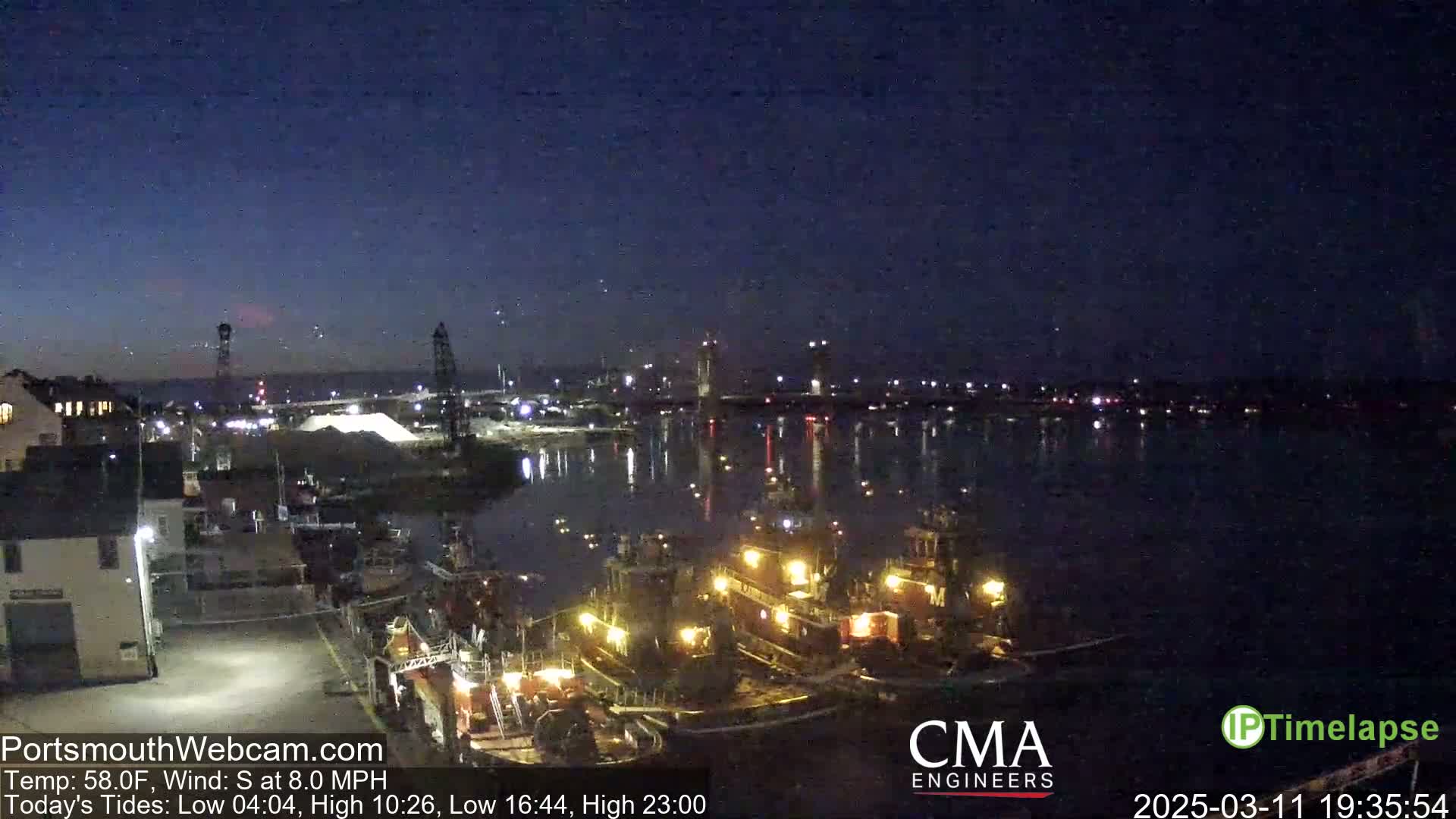 Several tugboats are docked at a waterfront at night under a clear, dark sky with a slight south wind.
