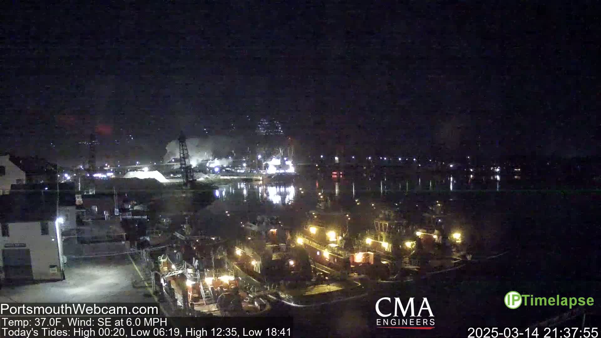 A nighttime harbor scene shows several docked tugboats illuminated under a clear, dark sky.
