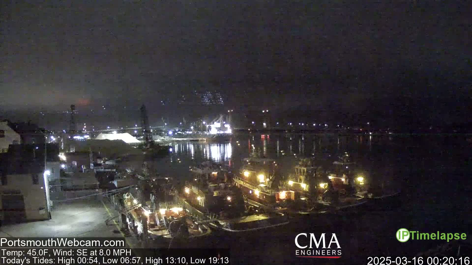 A nighttime view of a harbor with several tugboats docked, under a dark, overcast sky.