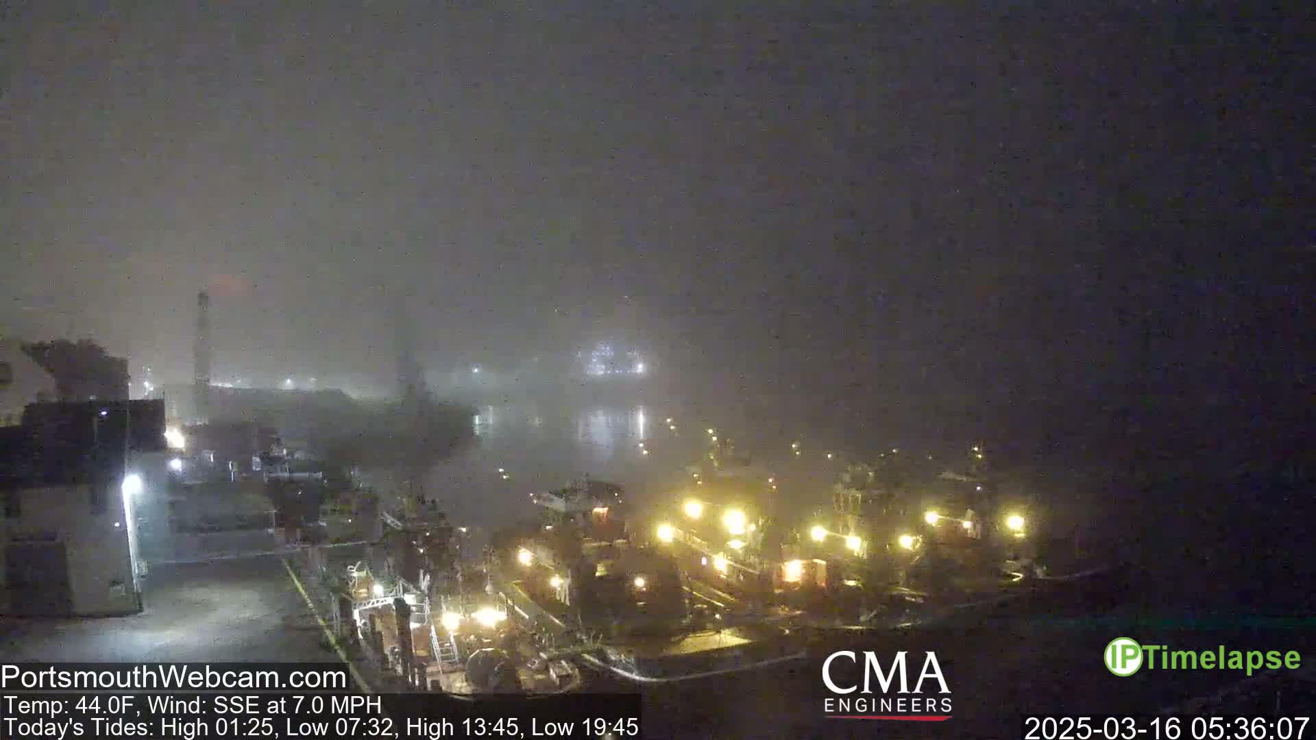 Several boats are docked at a wharf in a thick fog at night.