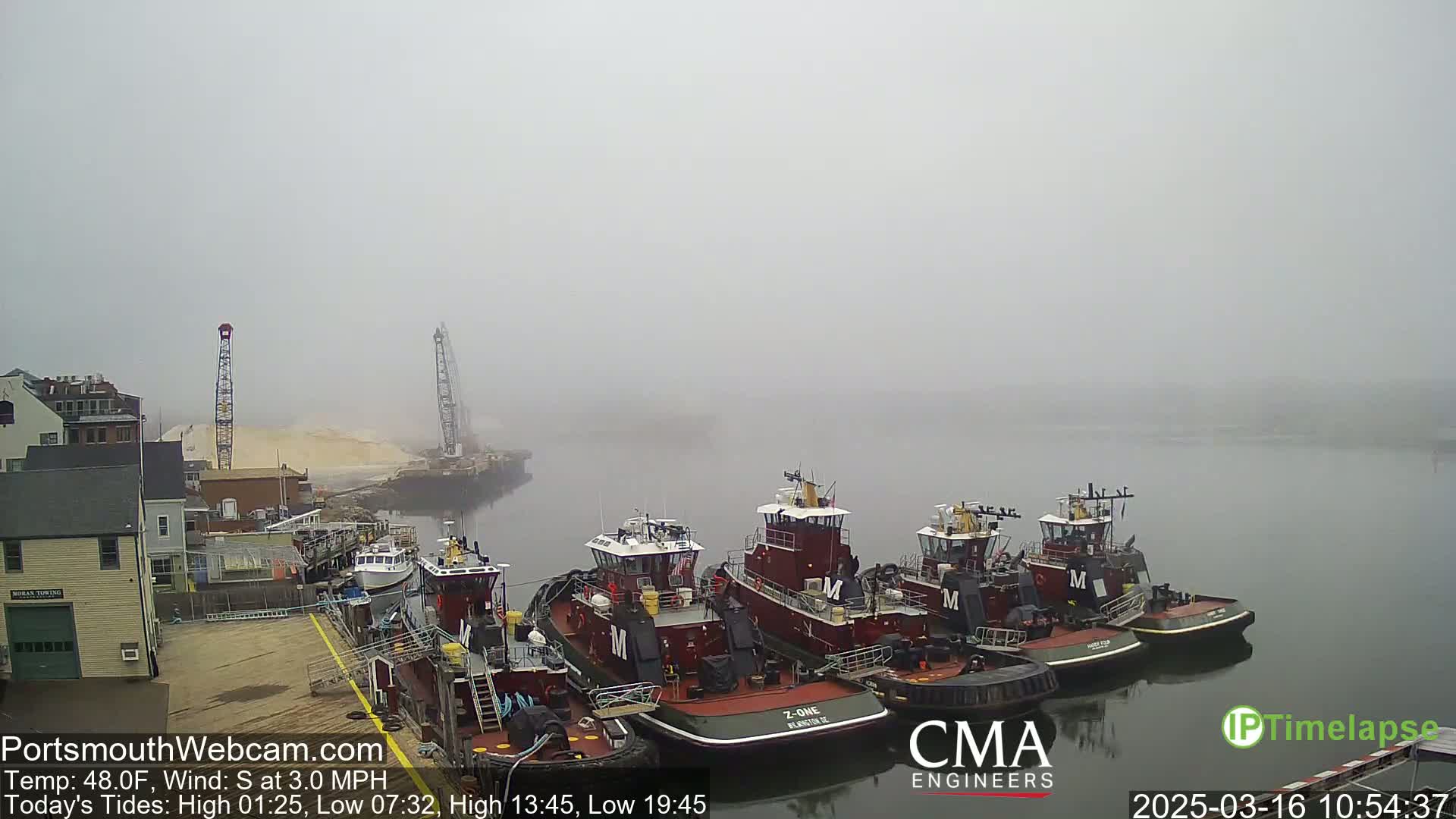 Several tugboats are moored at a dock in a foggy harbor.