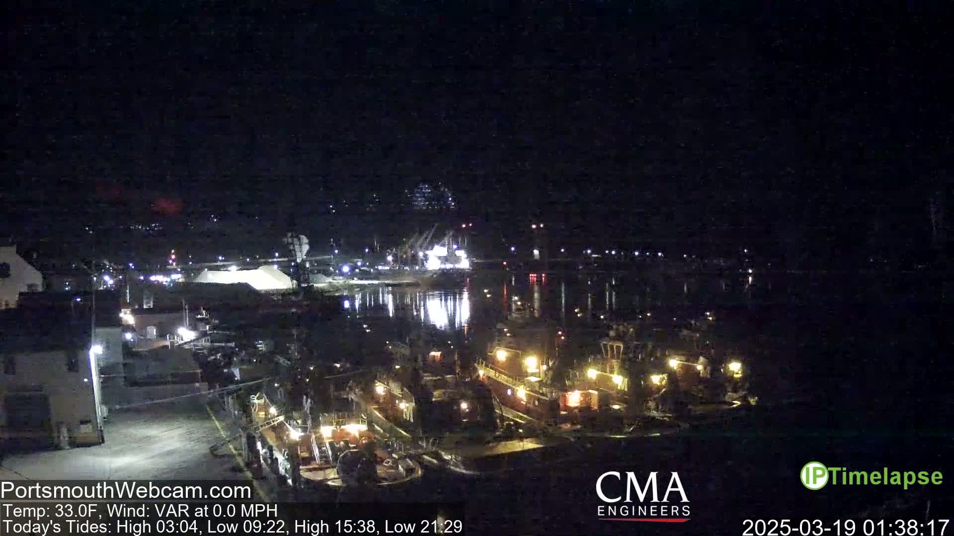Several illuminated tugboats are moored at a dock at night under a clear, dark sky.