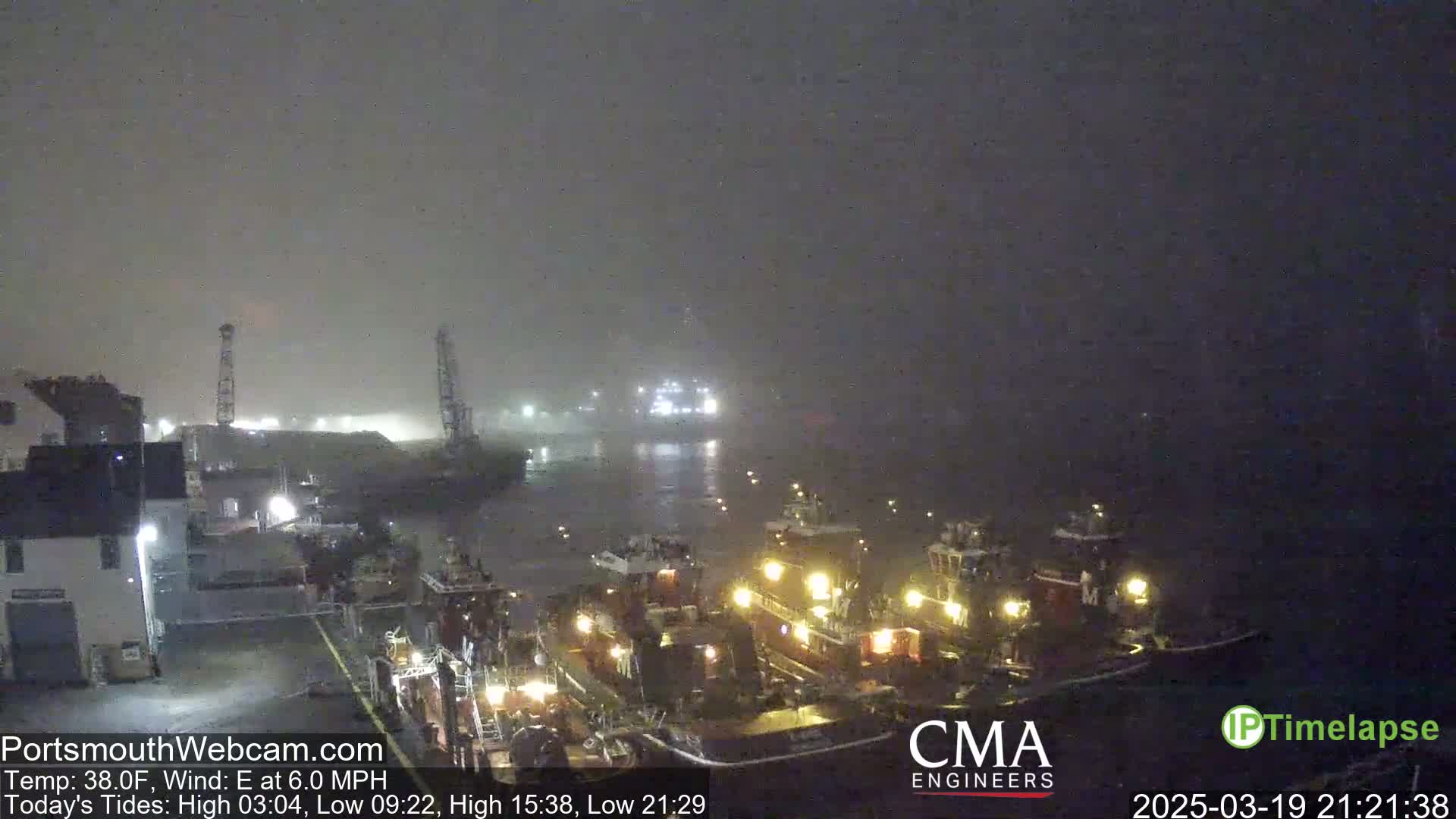 Several tugboats are docked at a harbor in foggy nighttime conditions.