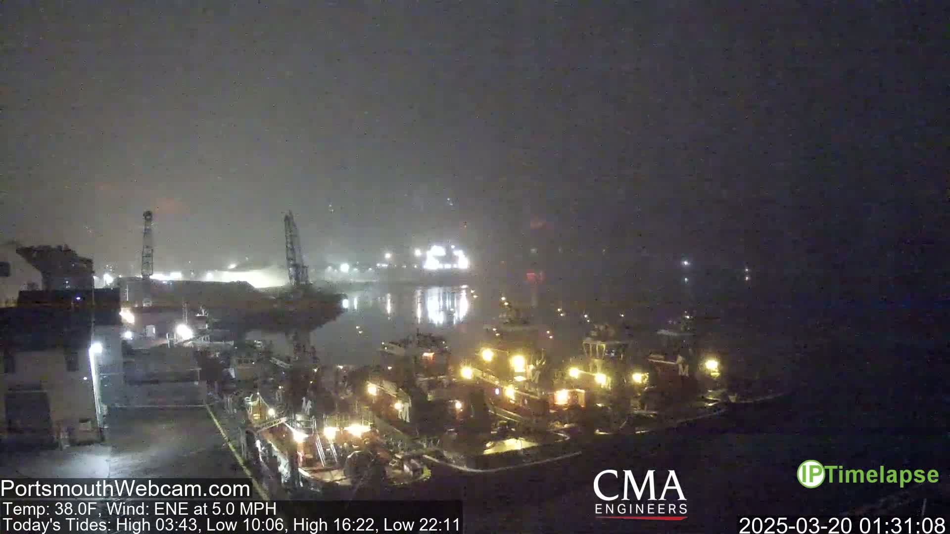 Several tugboats are docked at a nighttime harbor in foggy conditions.