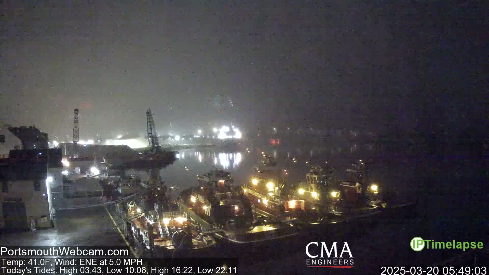 Several tugboats are moored at a dock in foggy nighttime conditions.