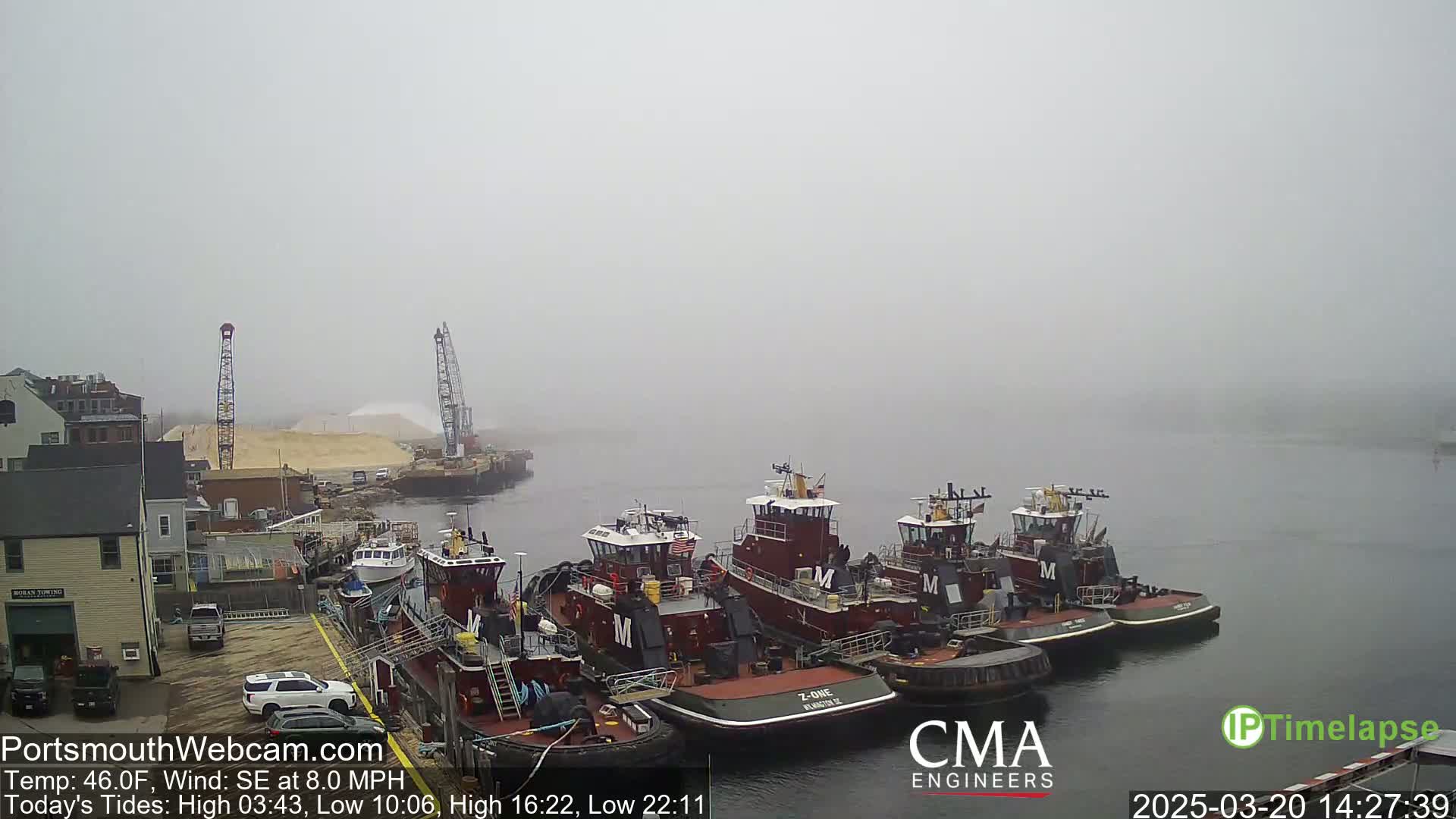 Several tugboats are docked at a wharf in foggy conditions.