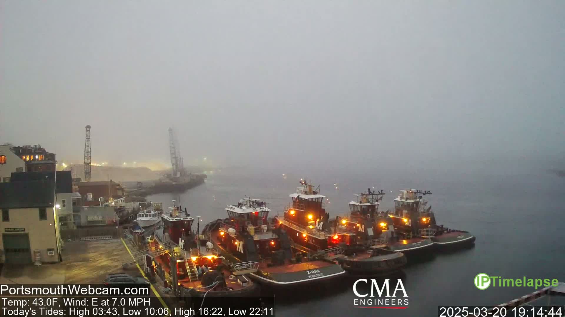 Several tugboats are docked at a wharf in foggy conditions.