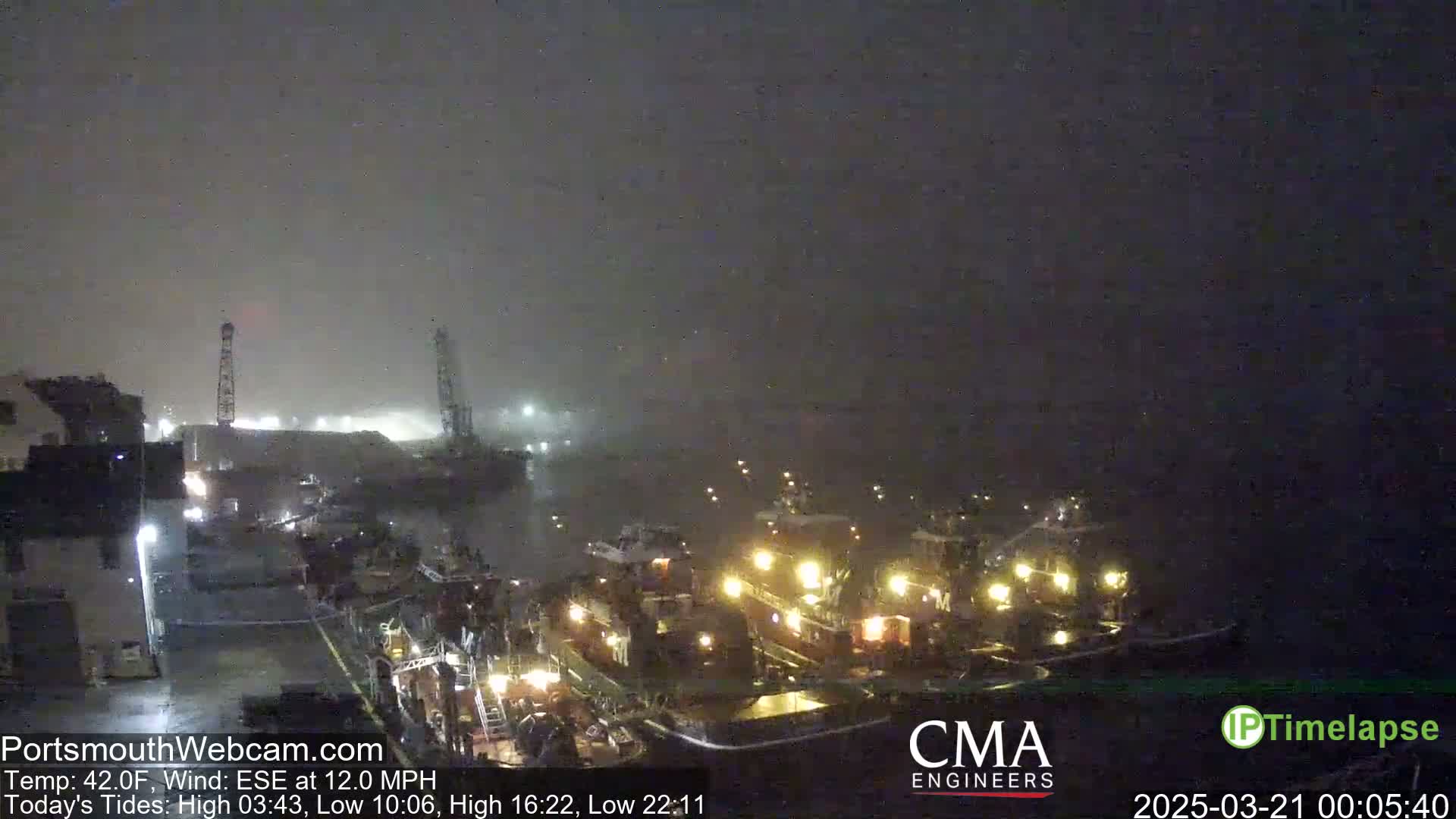A foggy night scene shows several tugboats docked at a port with a moderate wind.