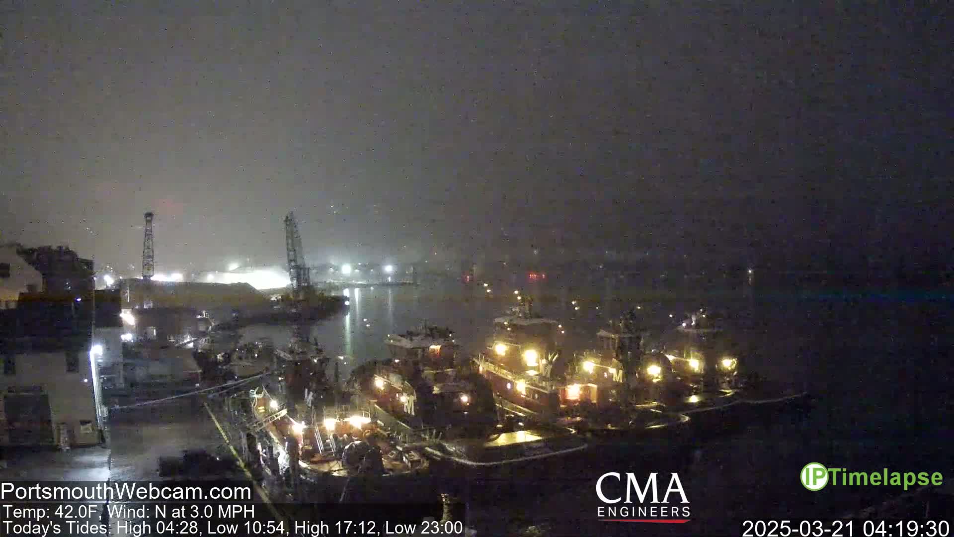 Several tugboats are moored at a dock at night in foggy conditions.