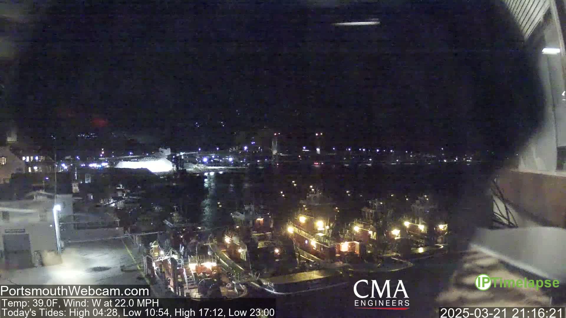 Several tugboats are docked at a harbor at night, under a dark sky with a west wind of 22 mph.
