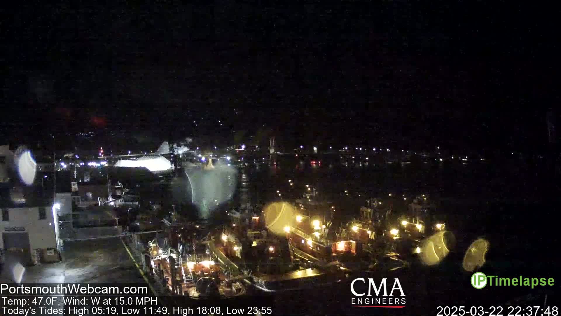 A nighttime harbor scene shows several docked boats illuminated by their lights under a dark, windy sky.