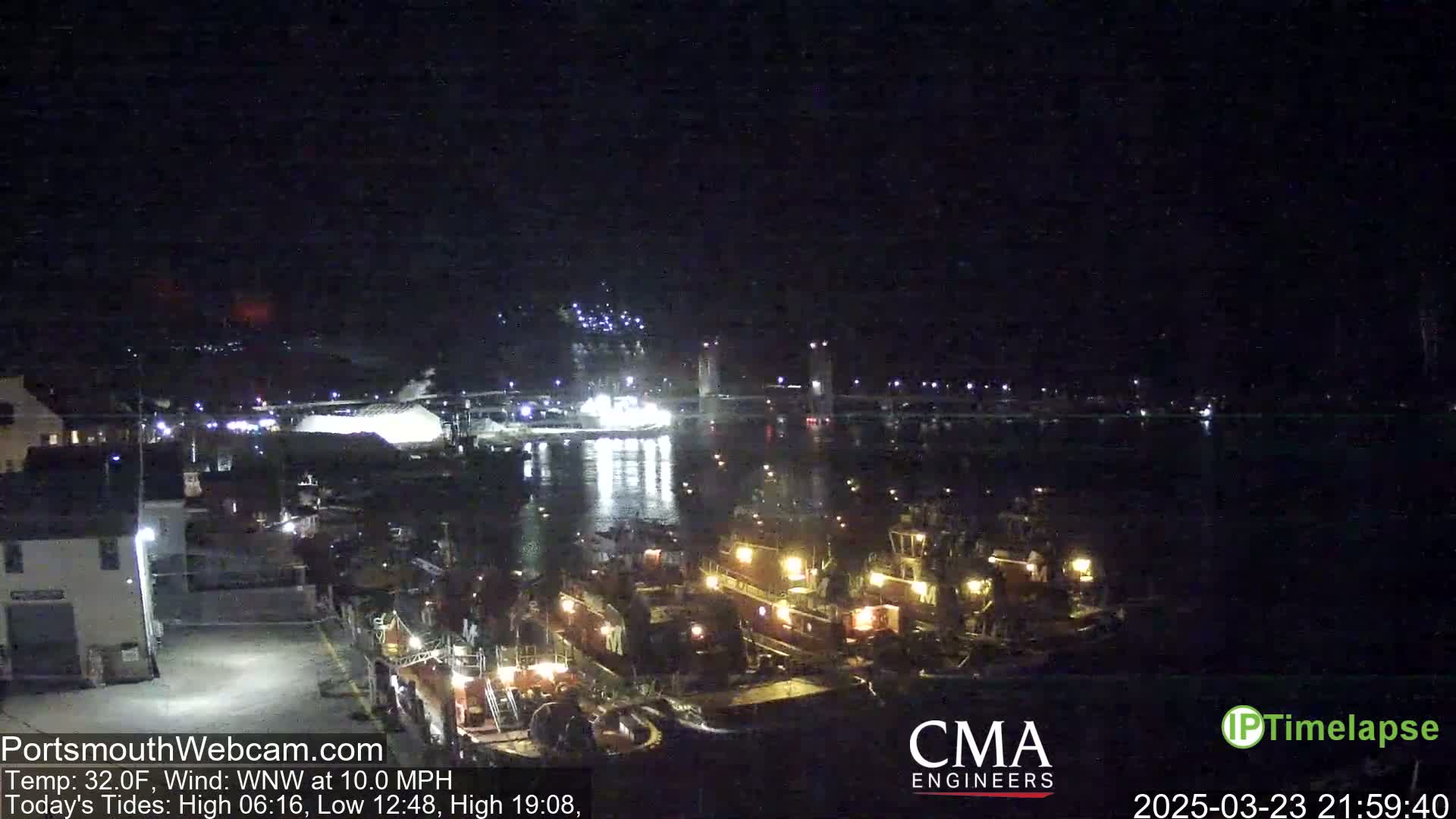 A nighttime, harbor scene with several tugboats docked near a bridge under a dark sky with a WNW wind at 10.0 mph and a temperature of 32°F.