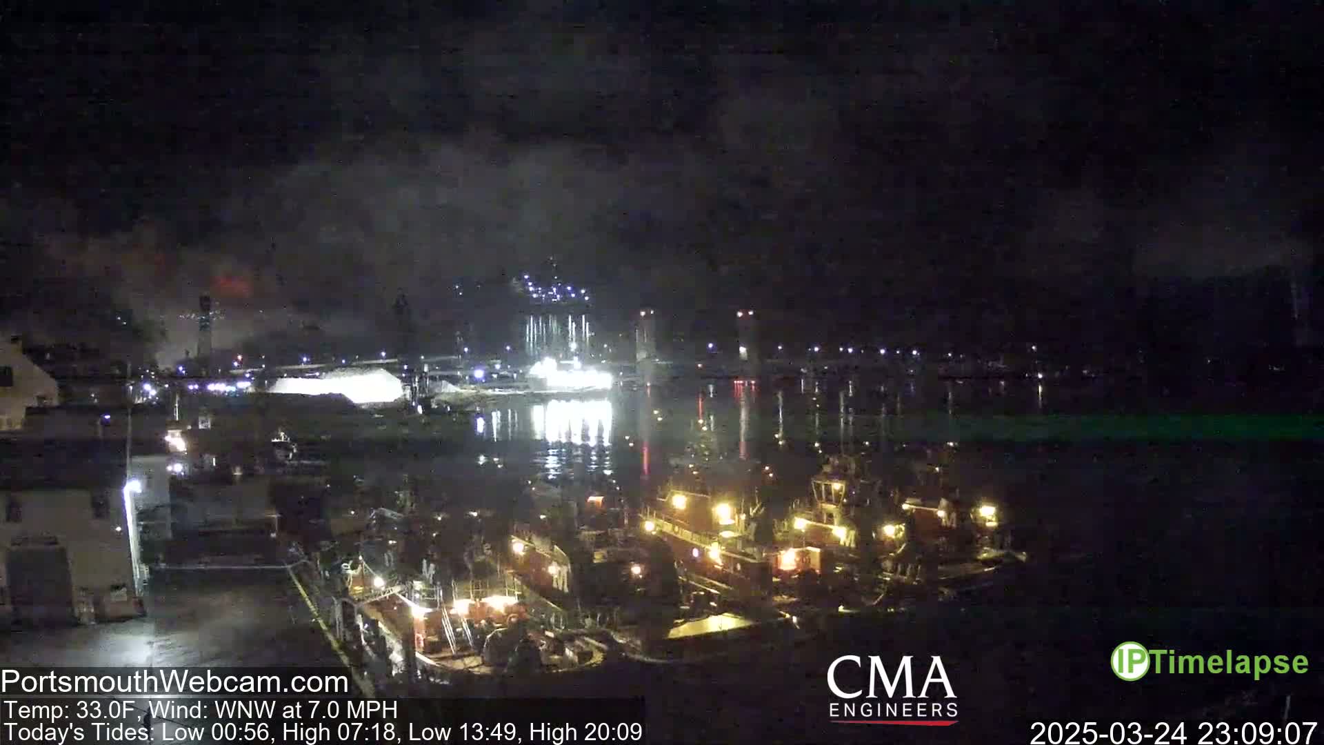 Several tugboats are moored at a nighttime dock under a dark, cloudy sky.