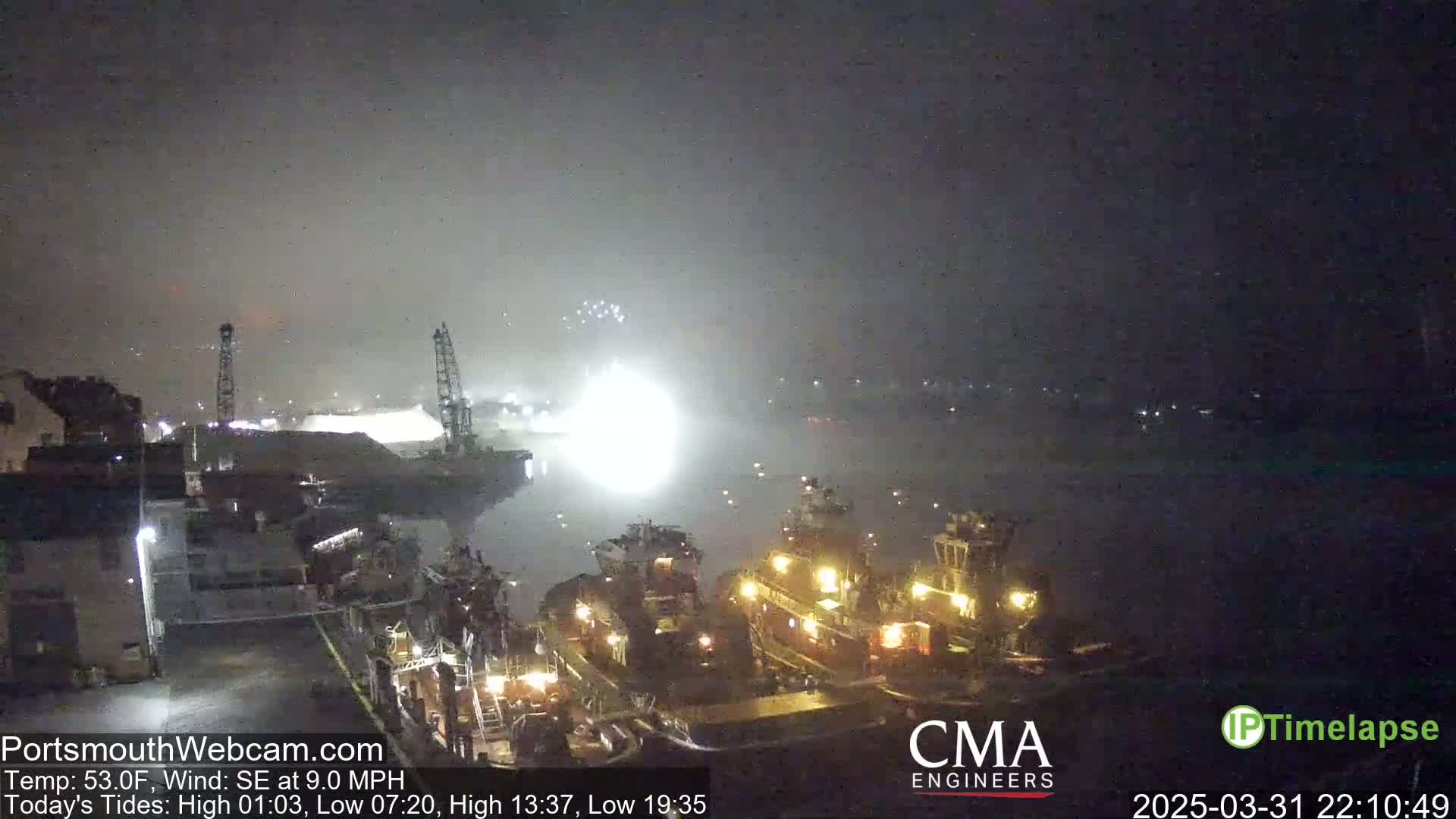 A nighttime harbor scene shows several tugboats moored near a brightly lit dock under hazy conditions with a southeast wind.