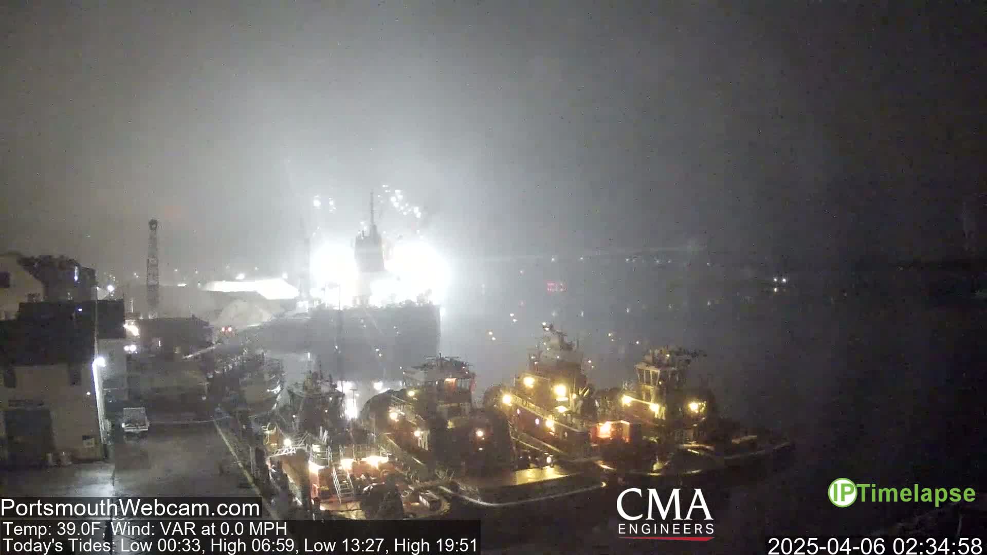 A large ship is being assisted by several tugboats in a foggy, nighttime harbor.