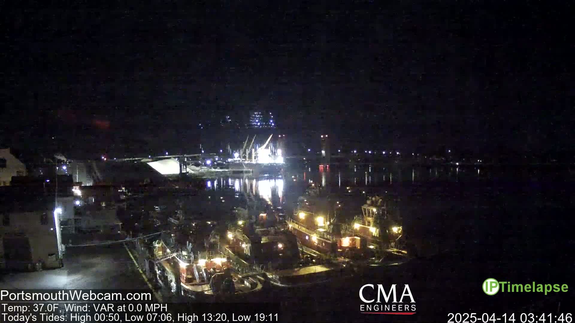 At night, several tugboats are docked near a body of water under a clear, dark sky.