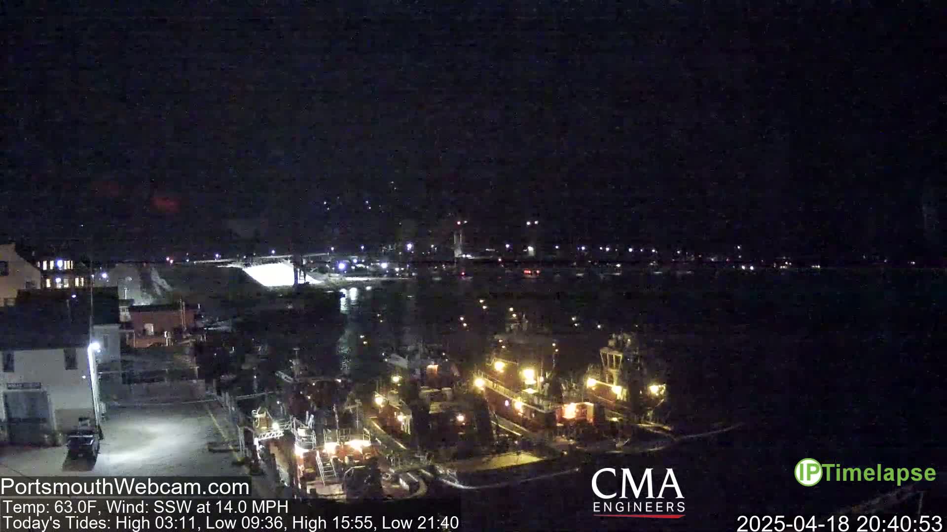 A nighttime view of a harbor with several docked tugboats illuminated under a dark sky.