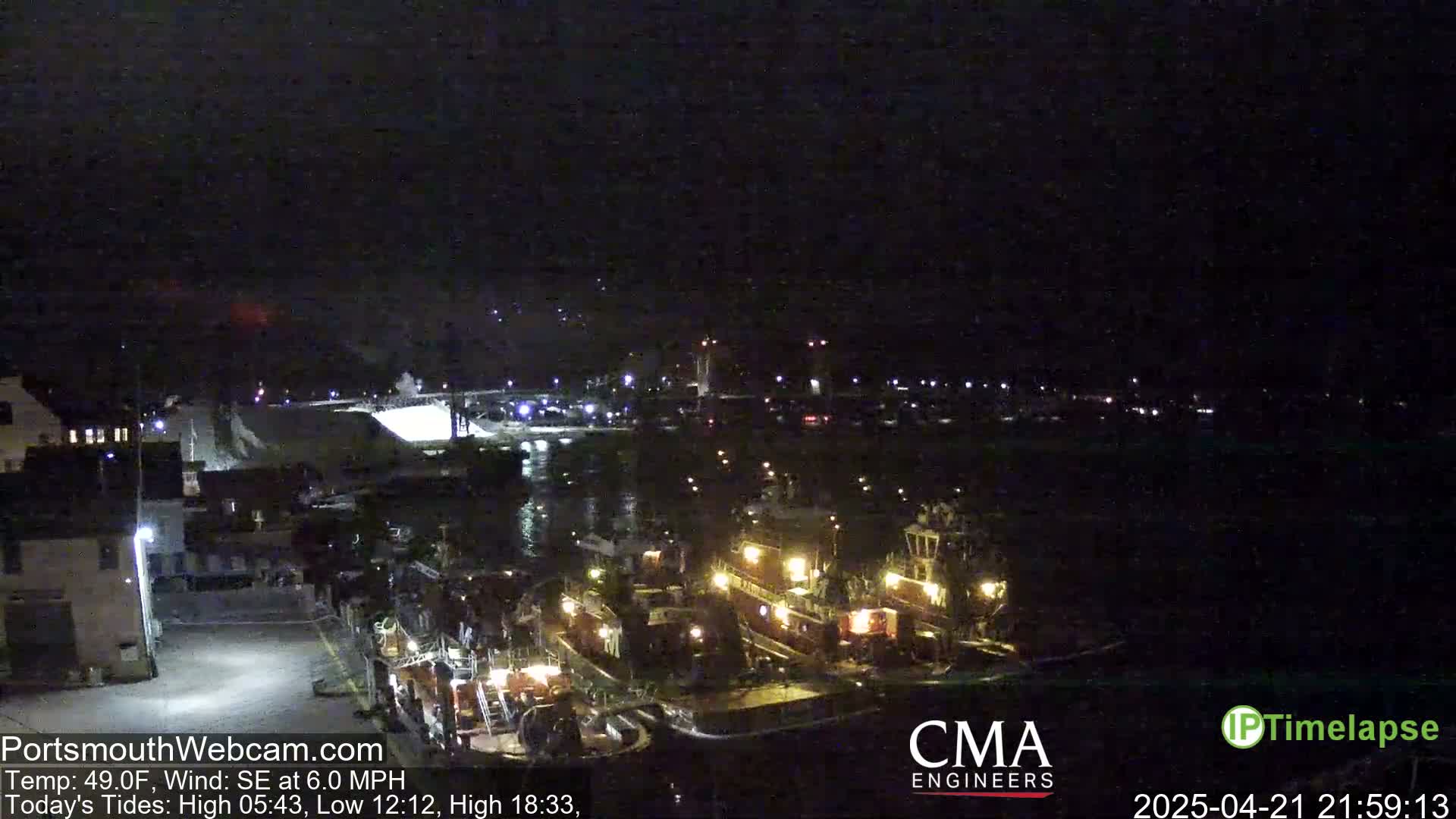 At night, several tugboats are docked near a shoreline, under a dark sky.