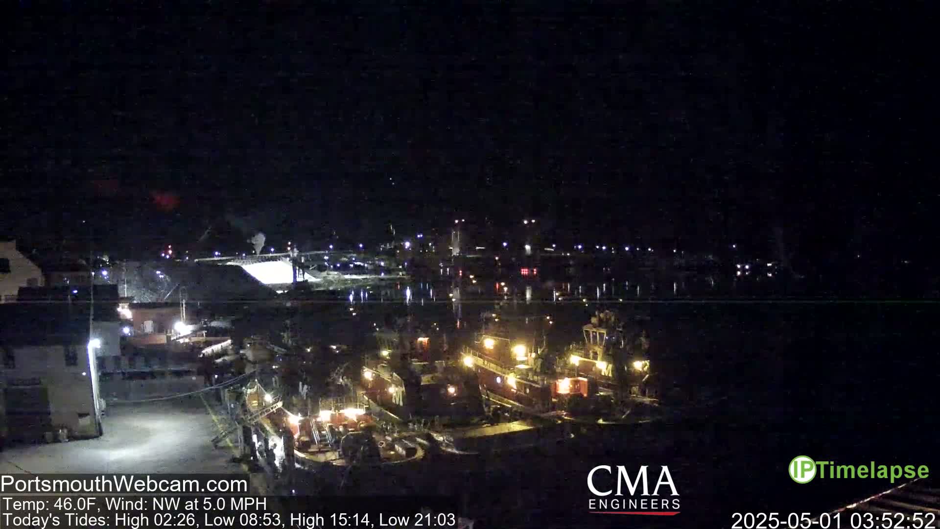 At night, several tugboats are docked near a waterfront, under a dark sky with a northwest wind.