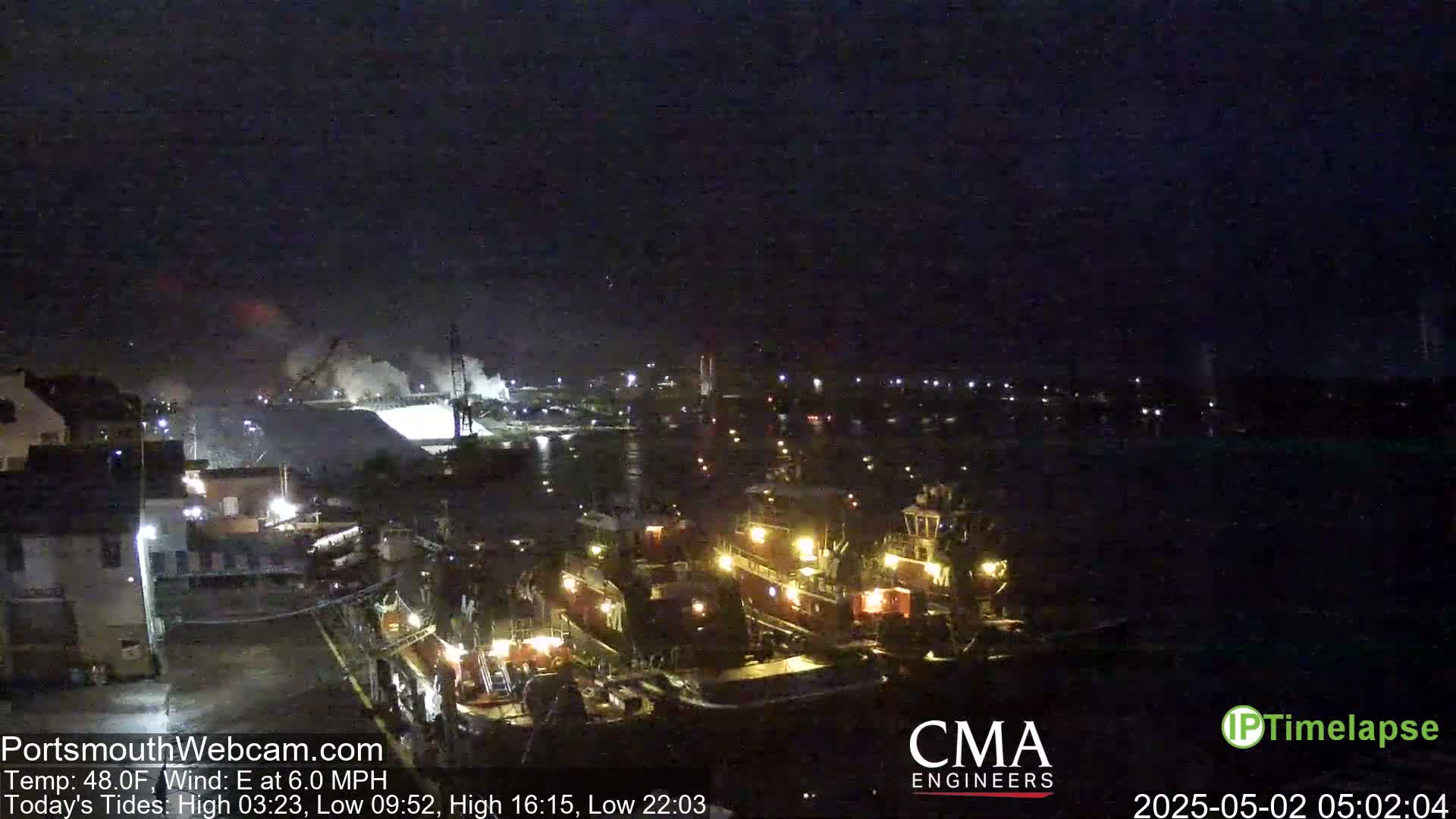 A nighttime harbor scene shows several tugboats illuminated by their lights, with a smoky haze in the distance under a dark sky.