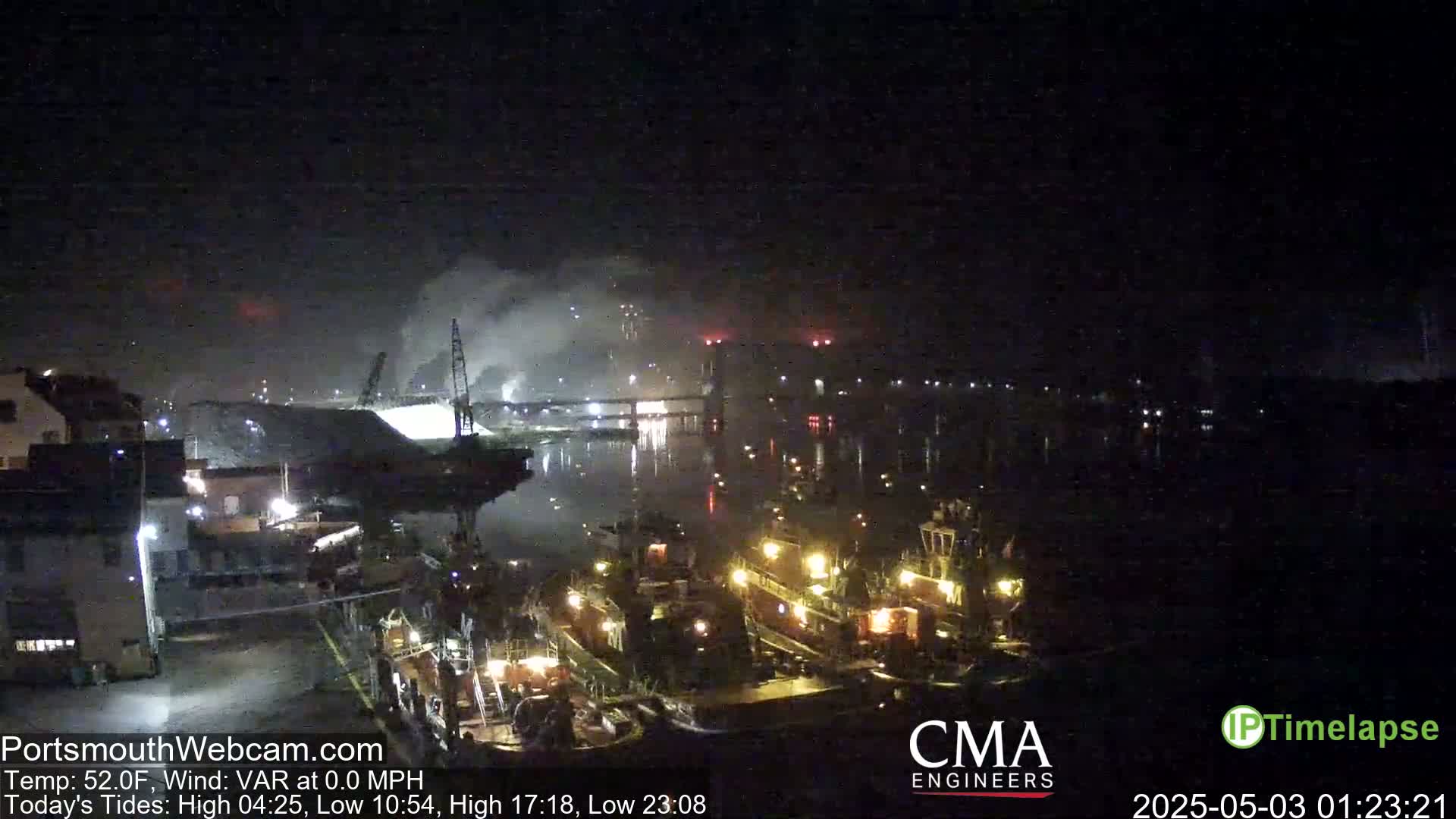 A nighttime view of a harbor with several tugboats, a large pile of material, and industrial cranes under a dark, clear sky.