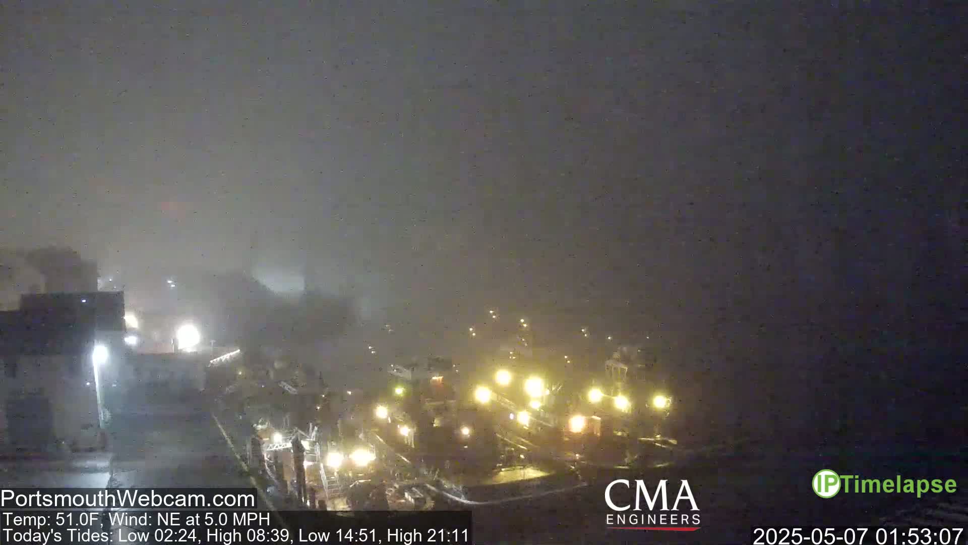 A foggy nighttime scene shows several docked boats with illuminated lights, in a harbor.