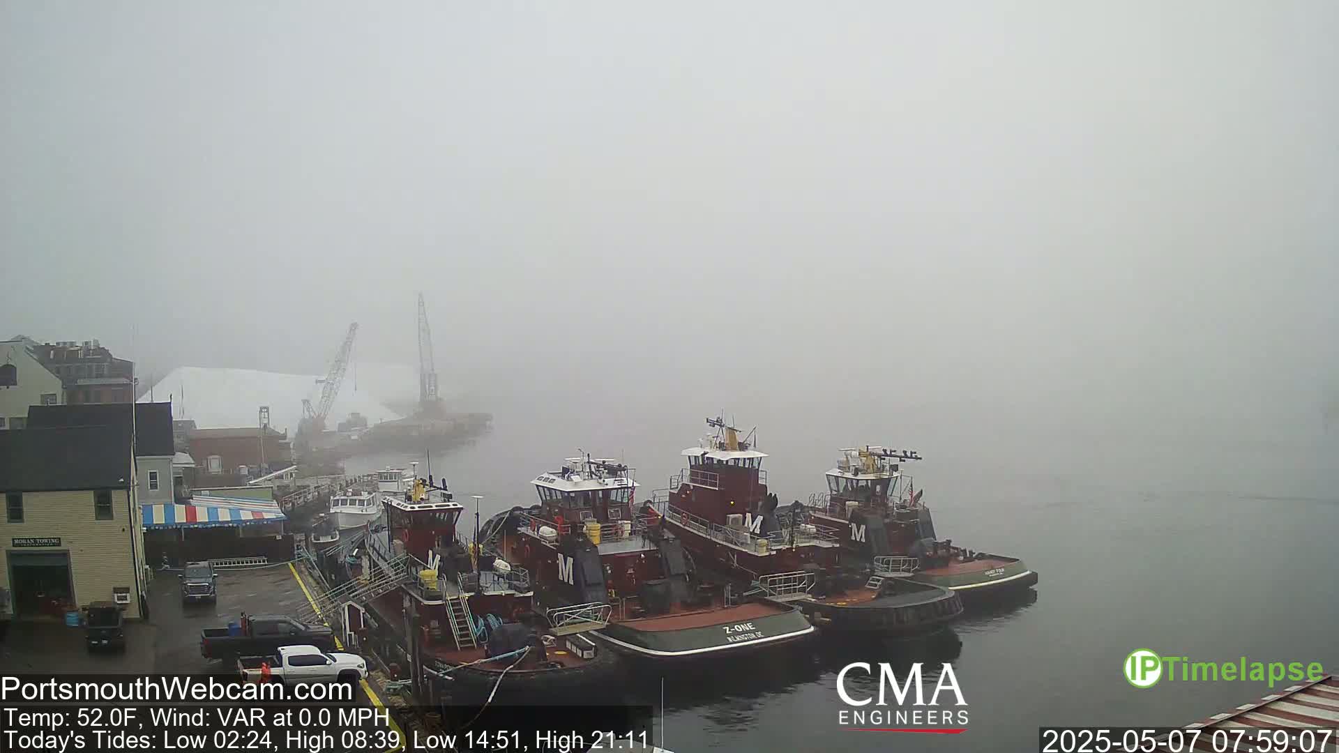 Several tugboats are moored at a dock in a thick fog.
