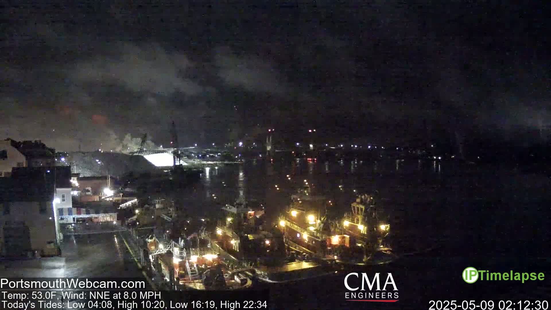 Several tugboats are docked at a nighttime harbor under a cloudy sky.
