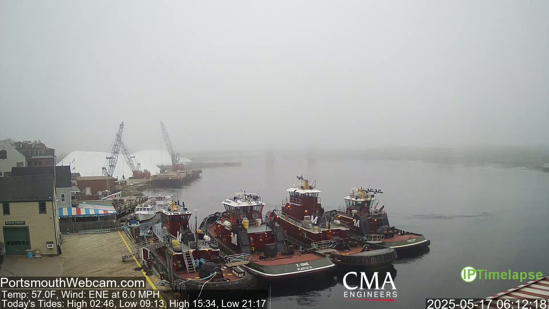 Several tugboats are moored at a dock in foggy conditions.
