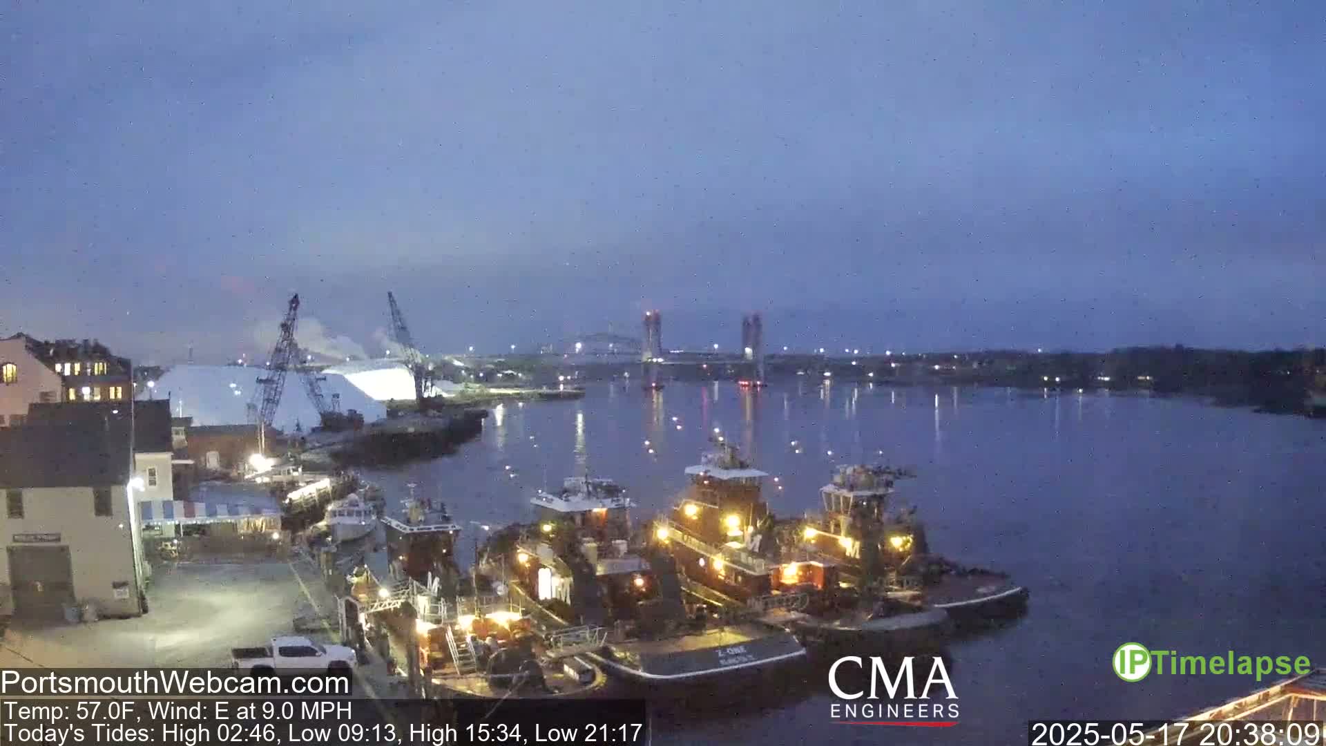 Several tugboats are moored at a dock next to a body of water at dusk, under a clear, twilight sky.