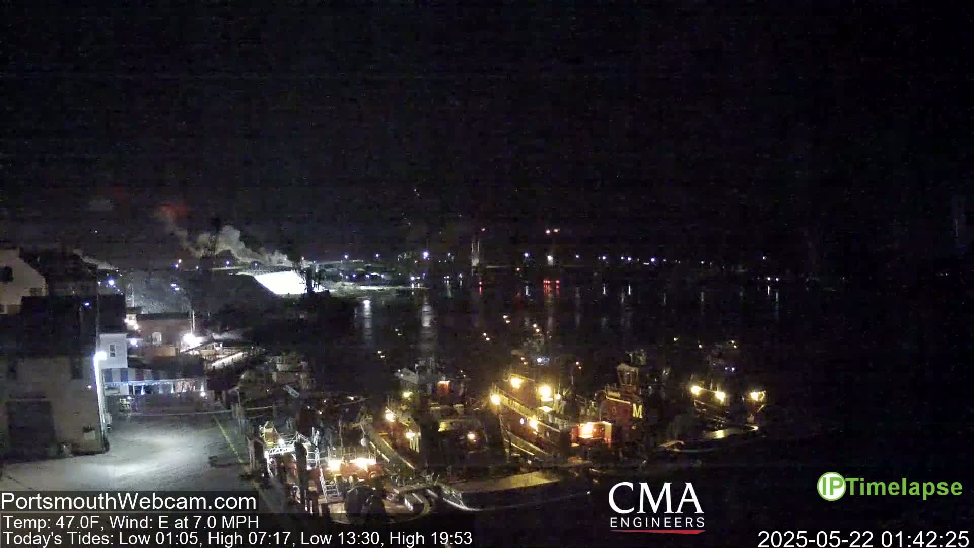 A nighttime view of a harbor with several tugboats docked, under a dark sky with a slight haze and an east wind.