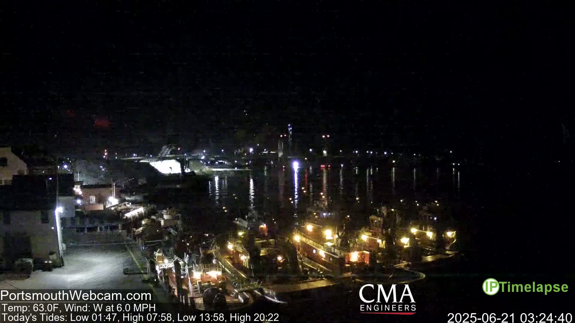 A nighttime harbor scene shows several docked fishing boats illuminated with lights, reflecting in calm water under a dark sky.