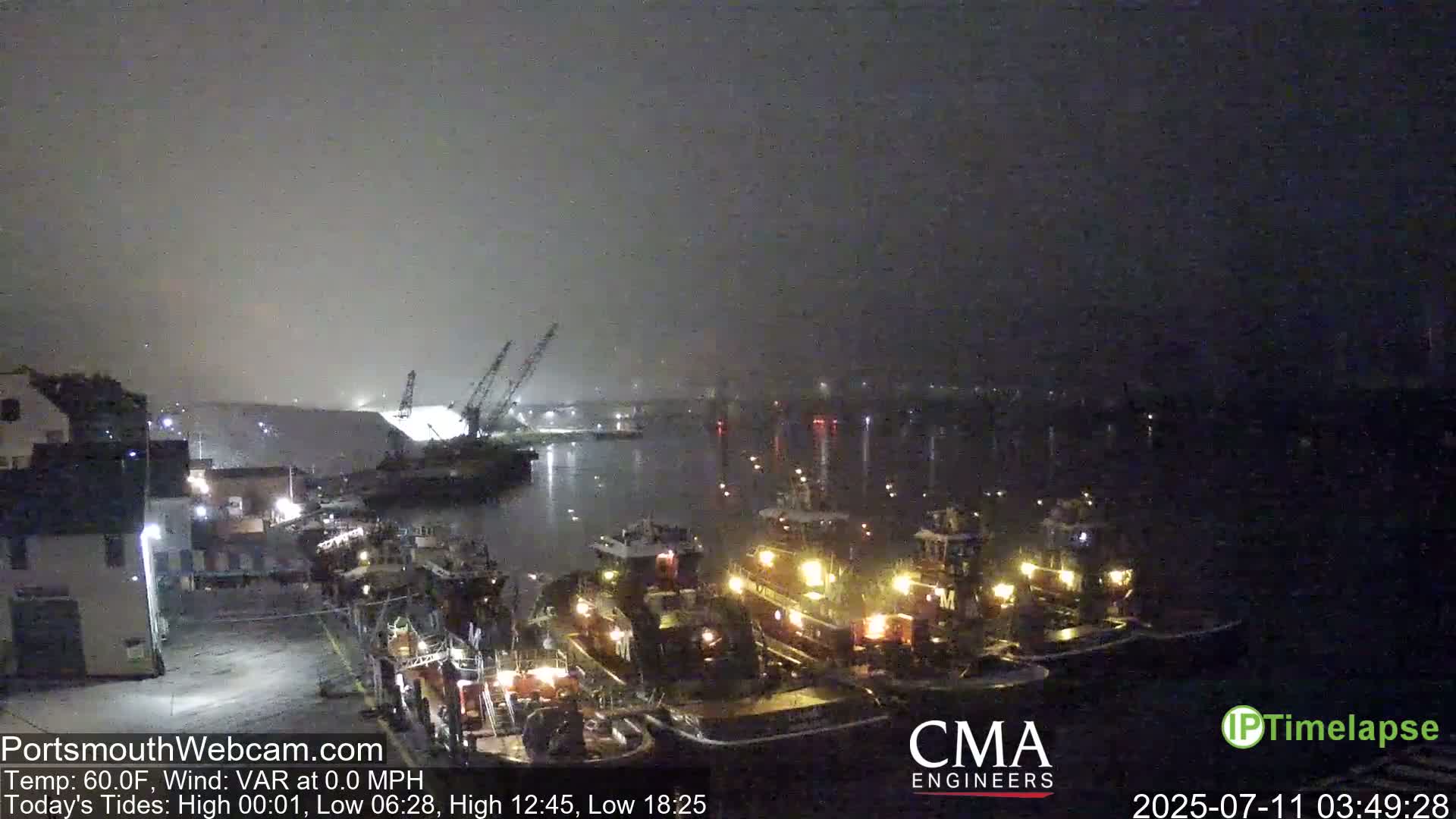 Several tugboats are moored at a dock at night in foggy conditions.