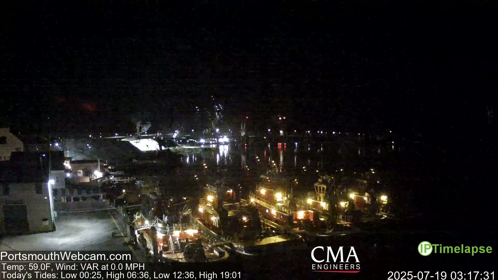 A nighttime harbor scene shows several tugboats docked, illuminated by their lights, under a clear, dark sky.