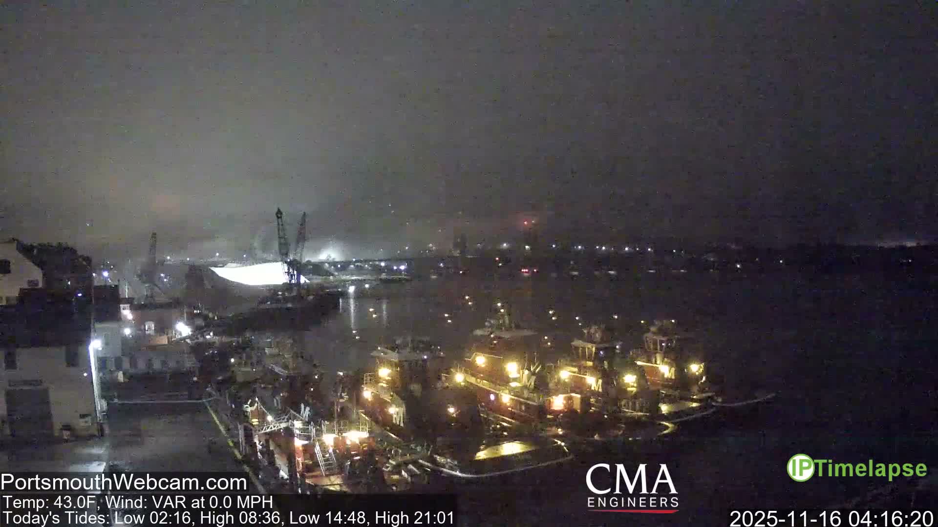 The image depicts a hazy, rain-speckled night over a busy industrial port, where numerous illuminated tugboats are docked and city lights reflect on the calm water.