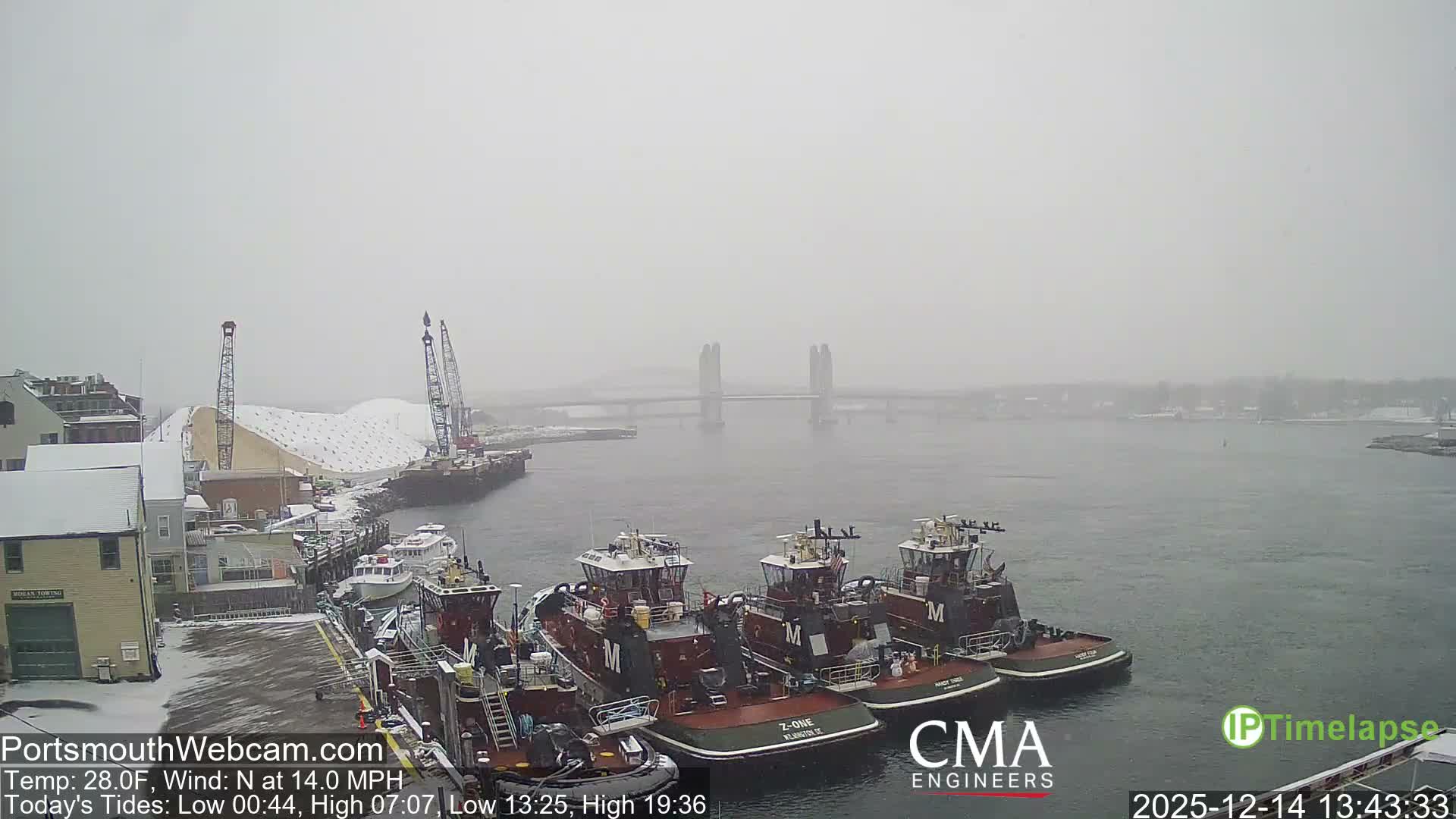 A bustling harbor at night is illuminated by numerous lights reflecting on the water, showing several boats docked and industrial structures on the shore, all under conditions of falling rain or snow.